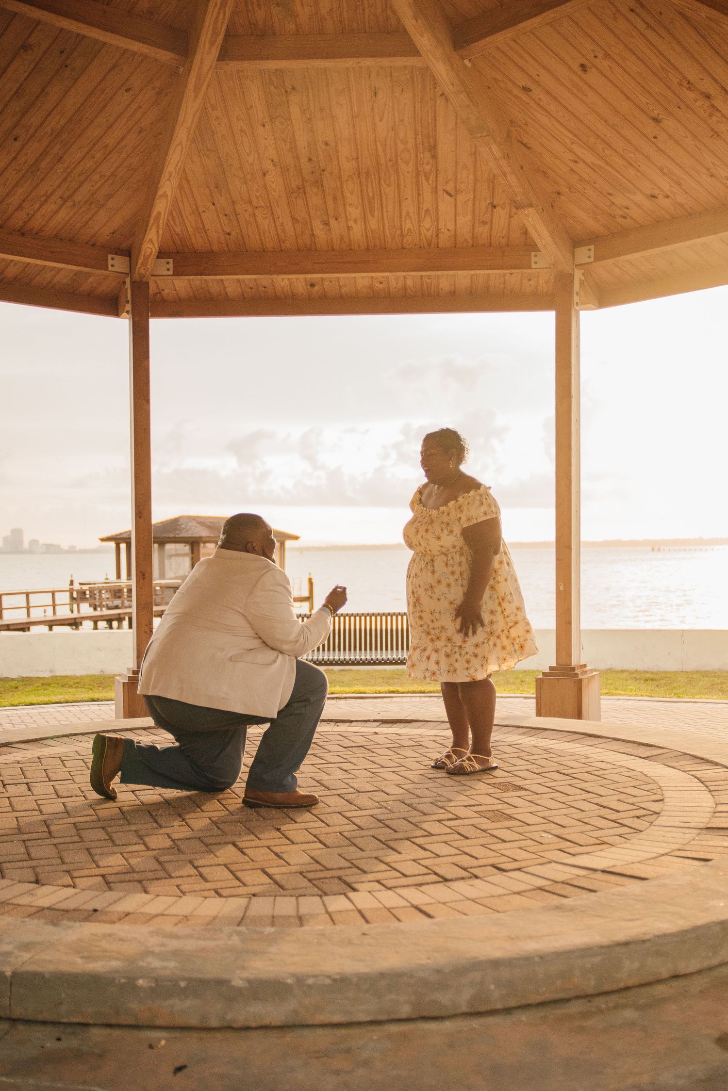 A romantic proposal moment under a wooden gazebo by the waterfront at sunset.