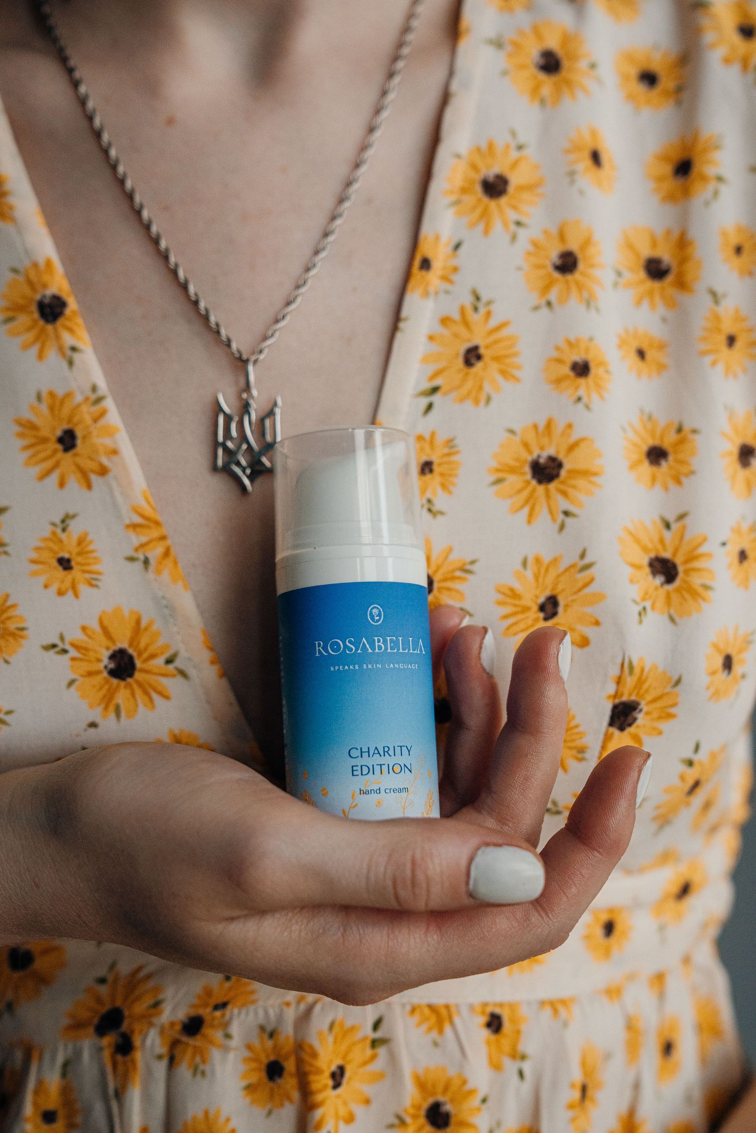 Person holding Rosabella Charity Edition hand cream wearing a floral sunflower dress.