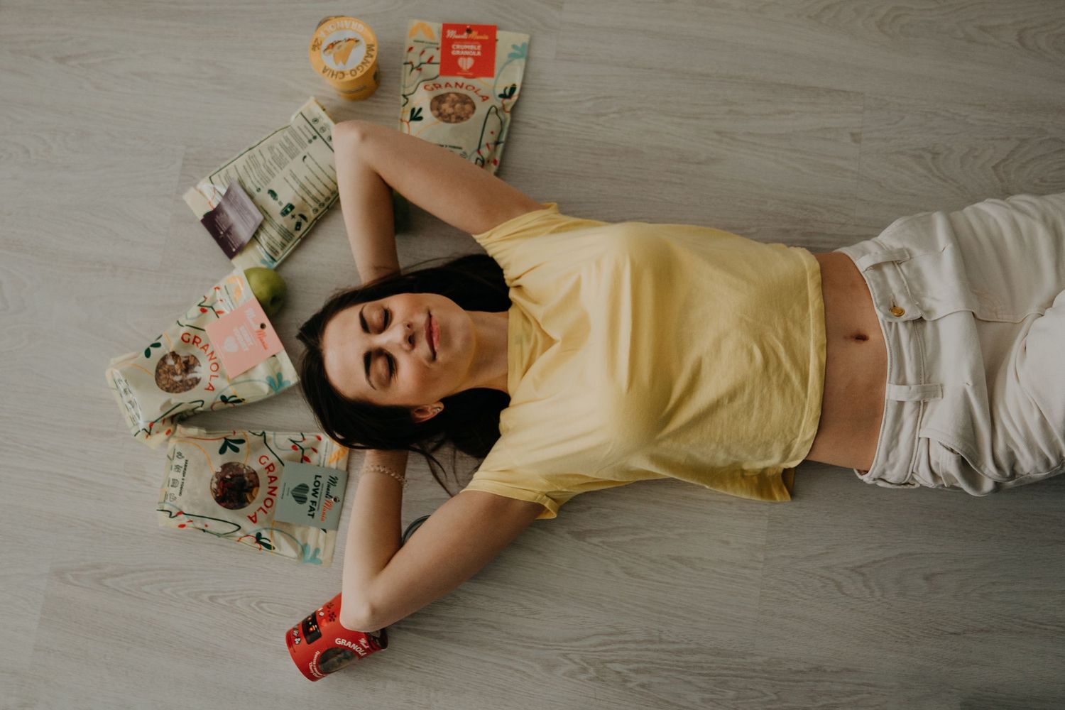 Young woman in yellow top lying on floor surrounded by colorful magazines and books, relaxing indoors.