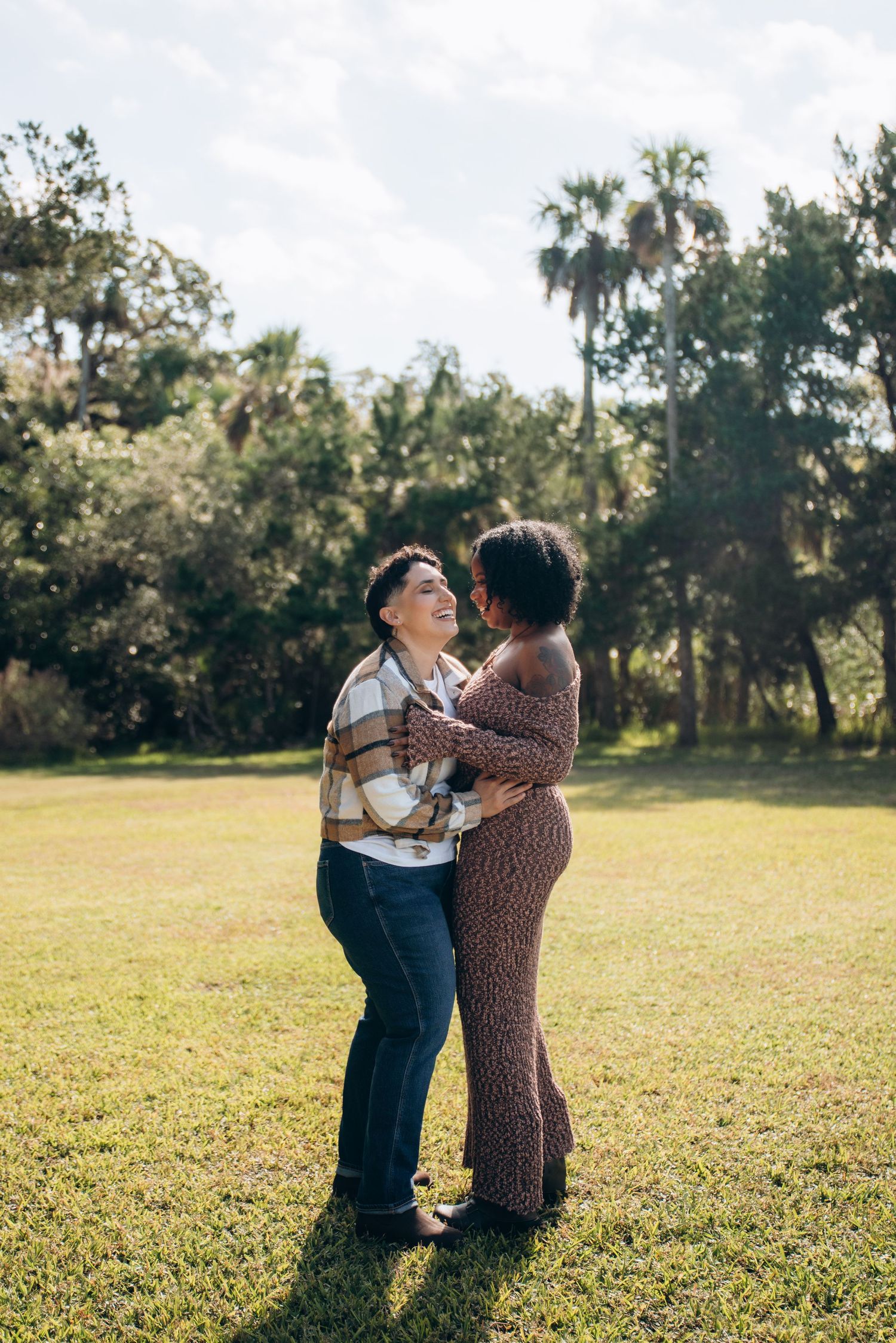 A romantic moment shared between two people standing in a sunny field with palm trees in the background.