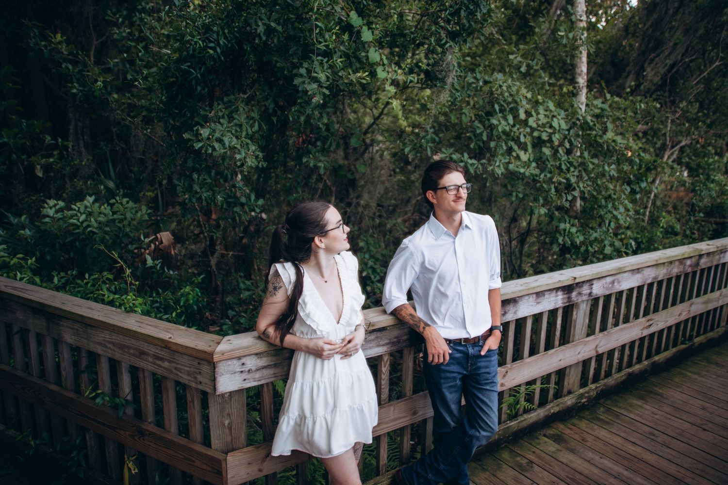 Couple embraces on a rustic wooden boardwalk surrounded by natural foliage.