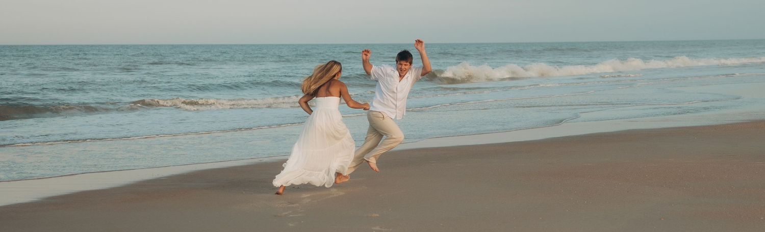 Couple strolling along the shoreline with waves crashing behind them.