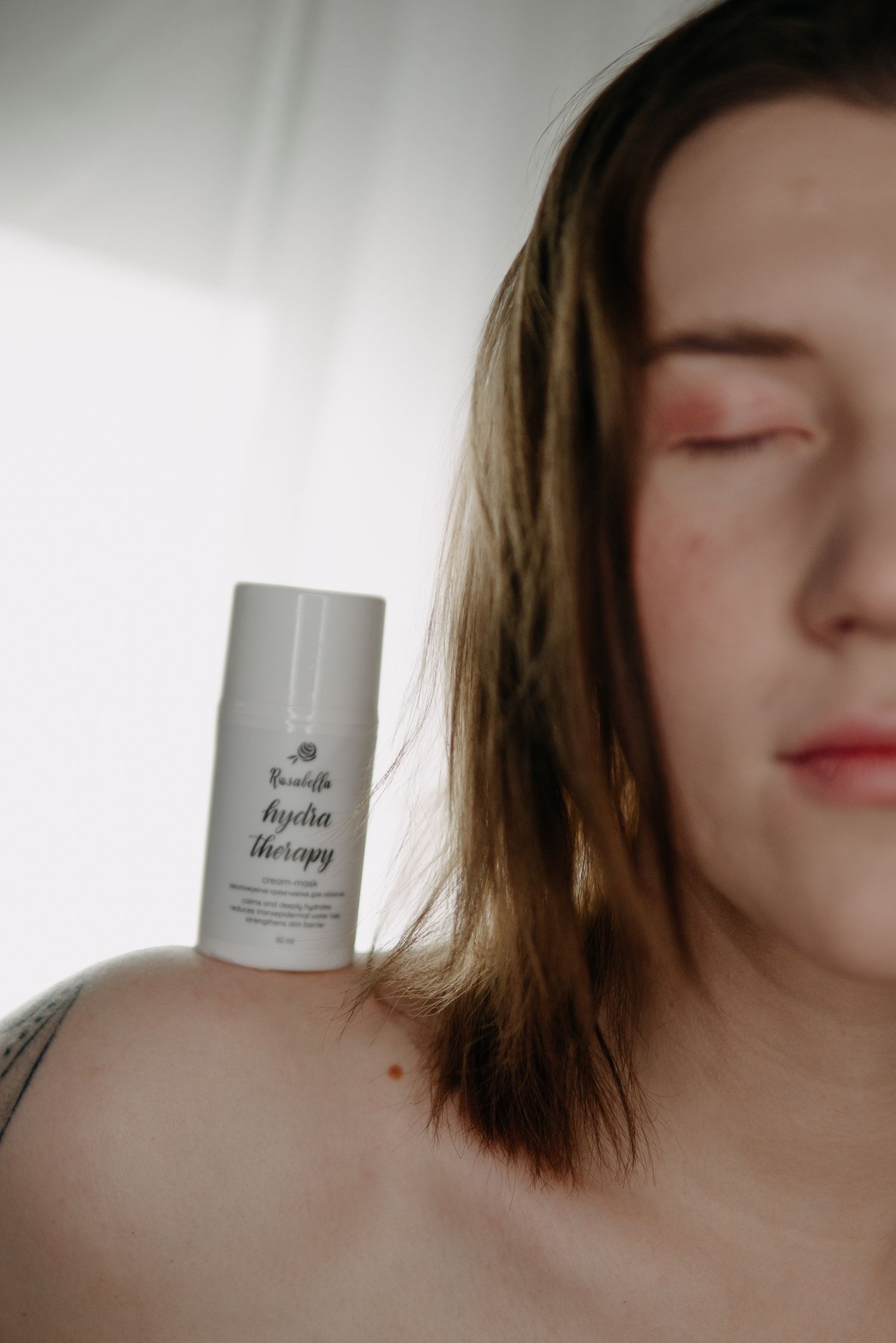 Woman with closed eyes holding Beautiffe Hydra Therapy skincare product against her shoulder in soft natural light.