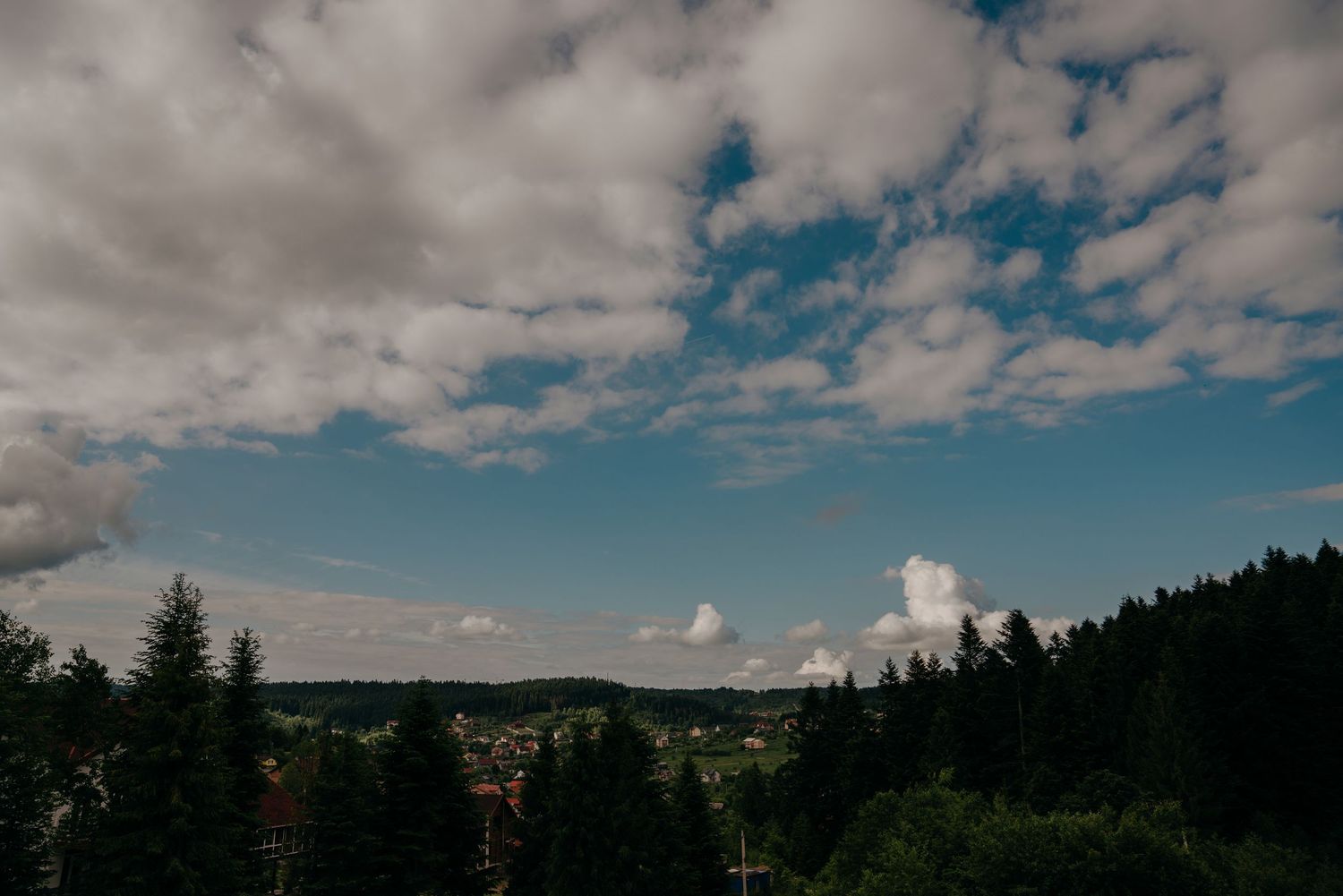 Scenic forest landscape with blue sky and white clouds over treetops in European countryside.