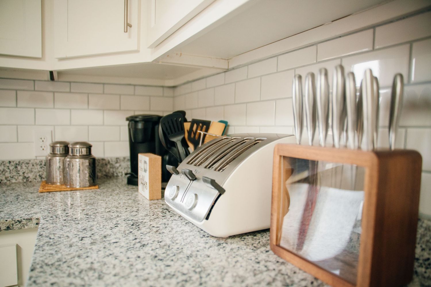 Kitchen counter with granite top, knife block, utensil holder, and white subway tile backsplash.