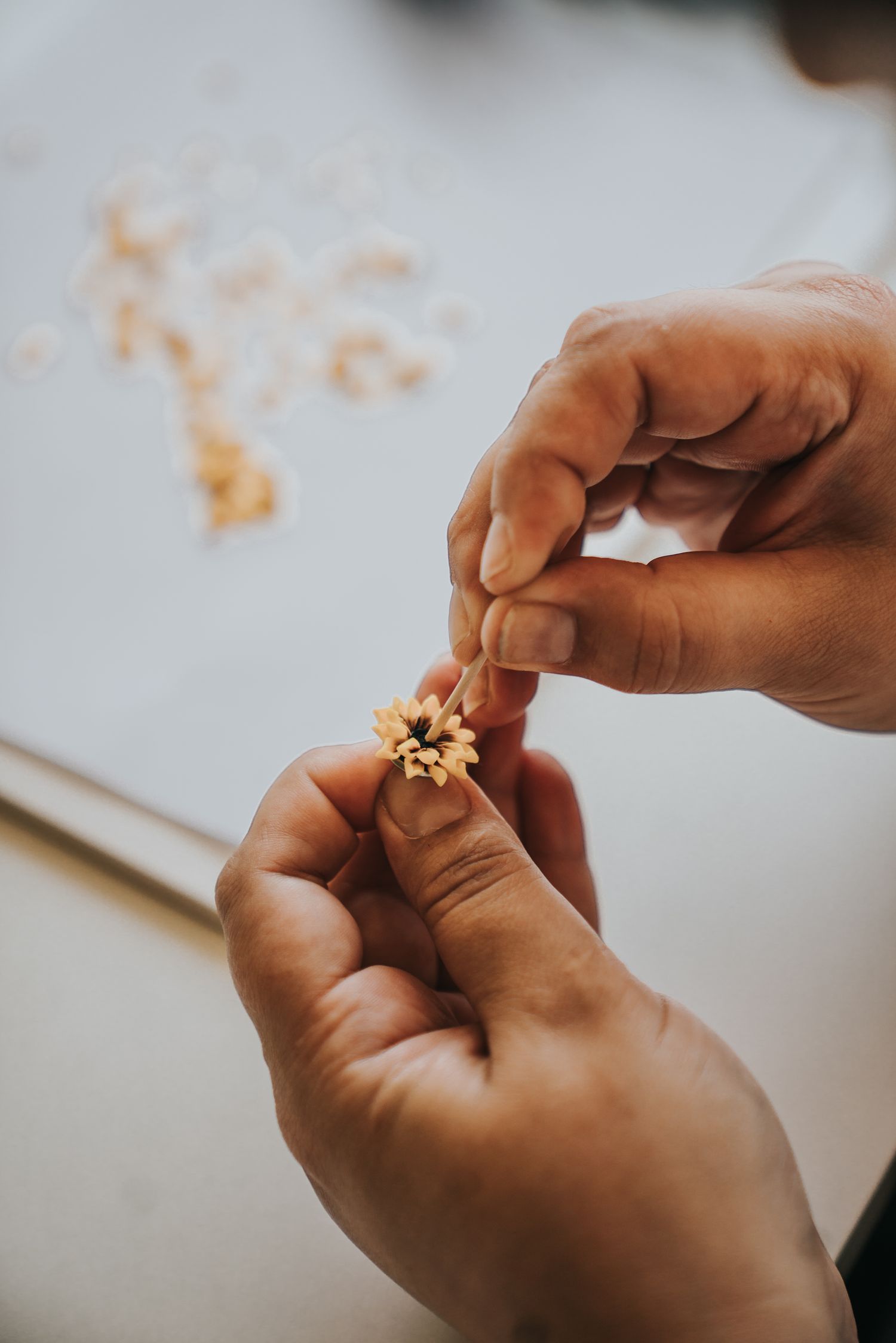 Hands carefully assembling a small handmade flower craft using natural materials on a white surface.