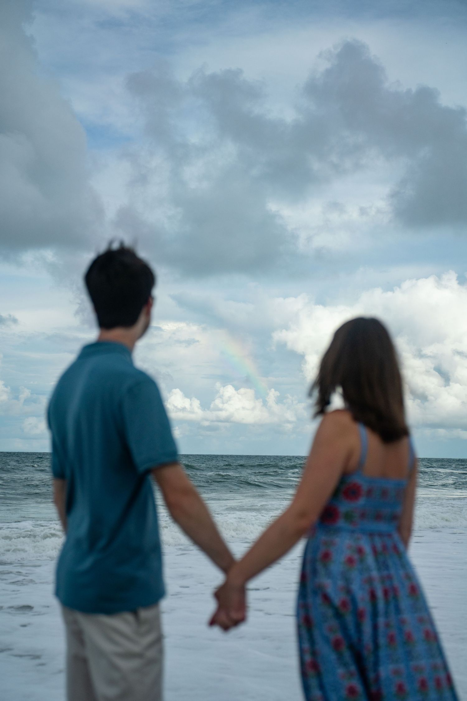 Silhouettes of a couple walking hand in hand along a moody beach at dusk.