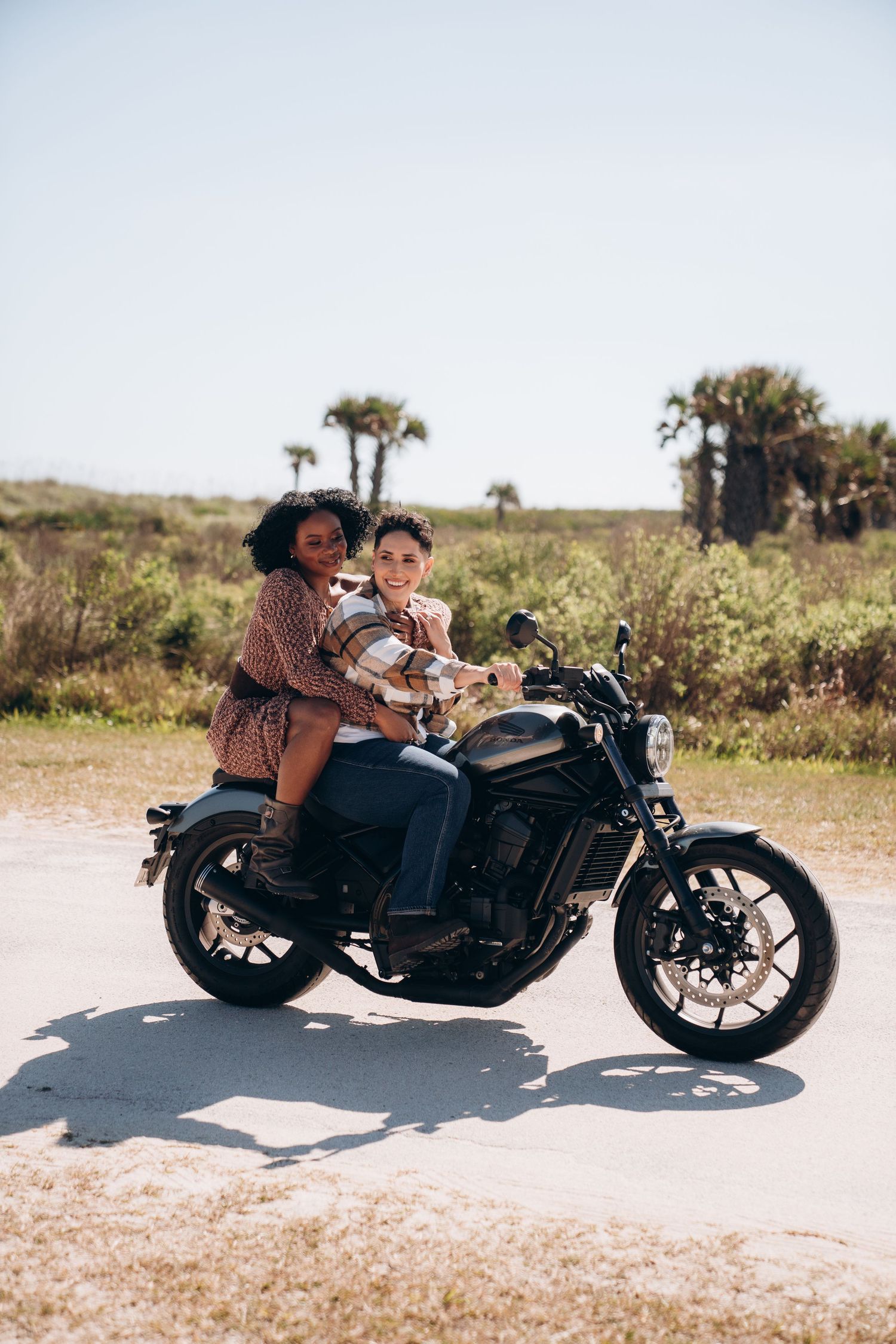 A motorcycle parked on a sandy beach path with palm trees in the distance.