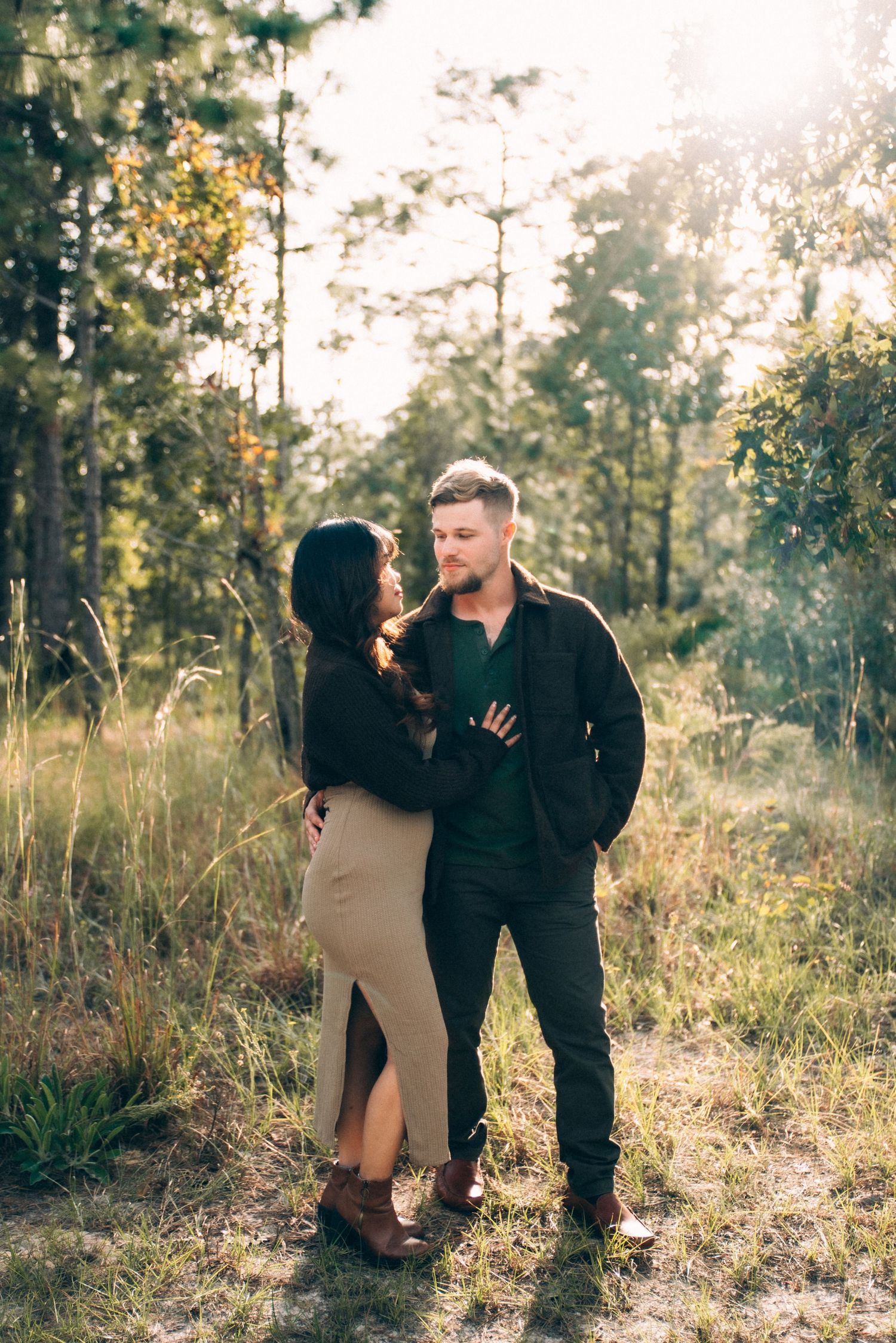 Couple shares tender moments in a sunlit forest clearing during golden hour.