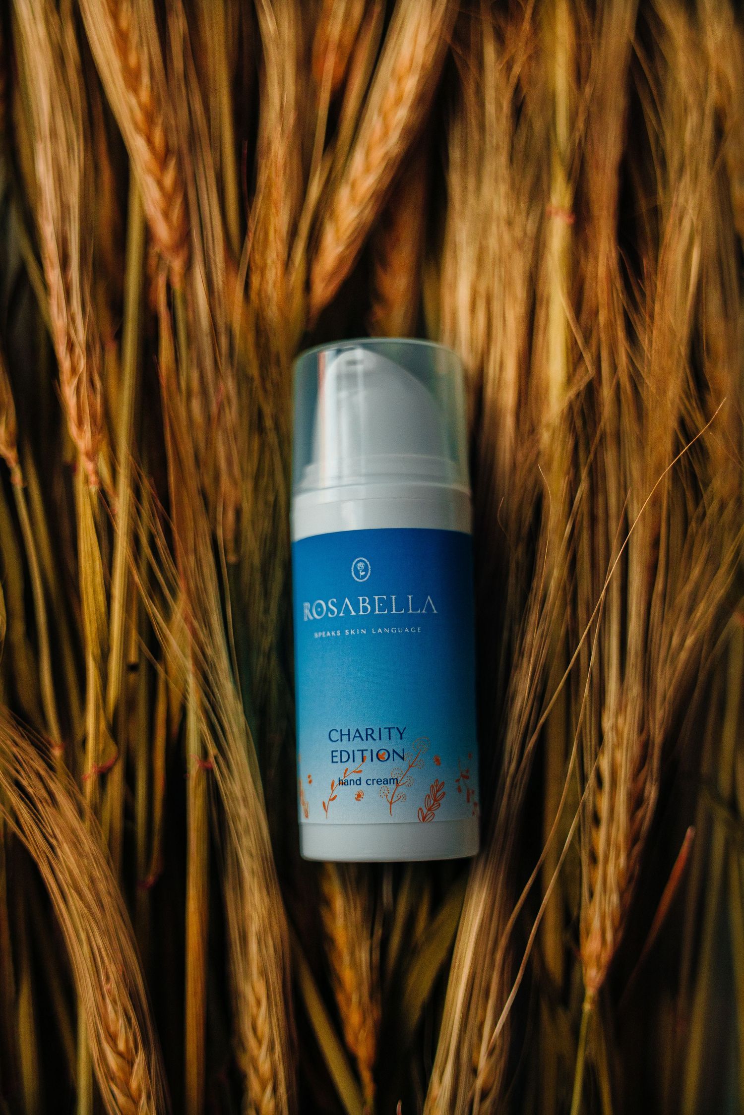 Rosabella Charity Edition hand cream pump bottle nestled among golden wheat stalks.