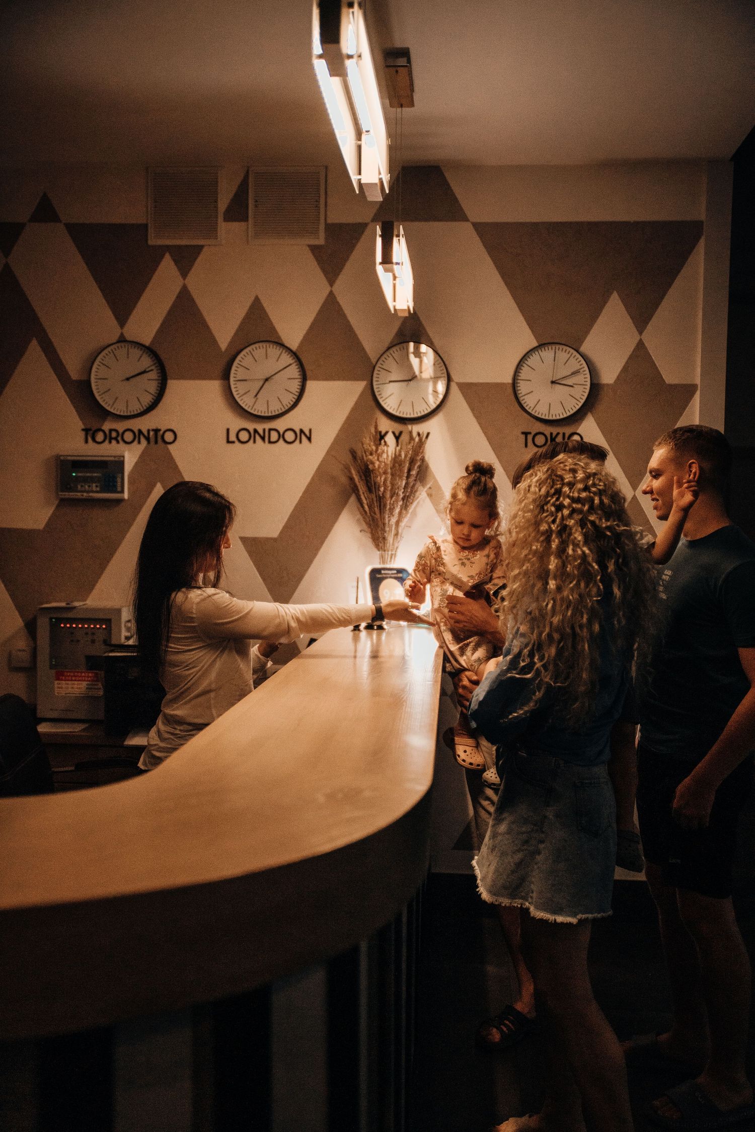 Family checking in at a hotel reception desk with world time zone clocks for Toronto, London, Kyiv, and Tokyo on the wall.