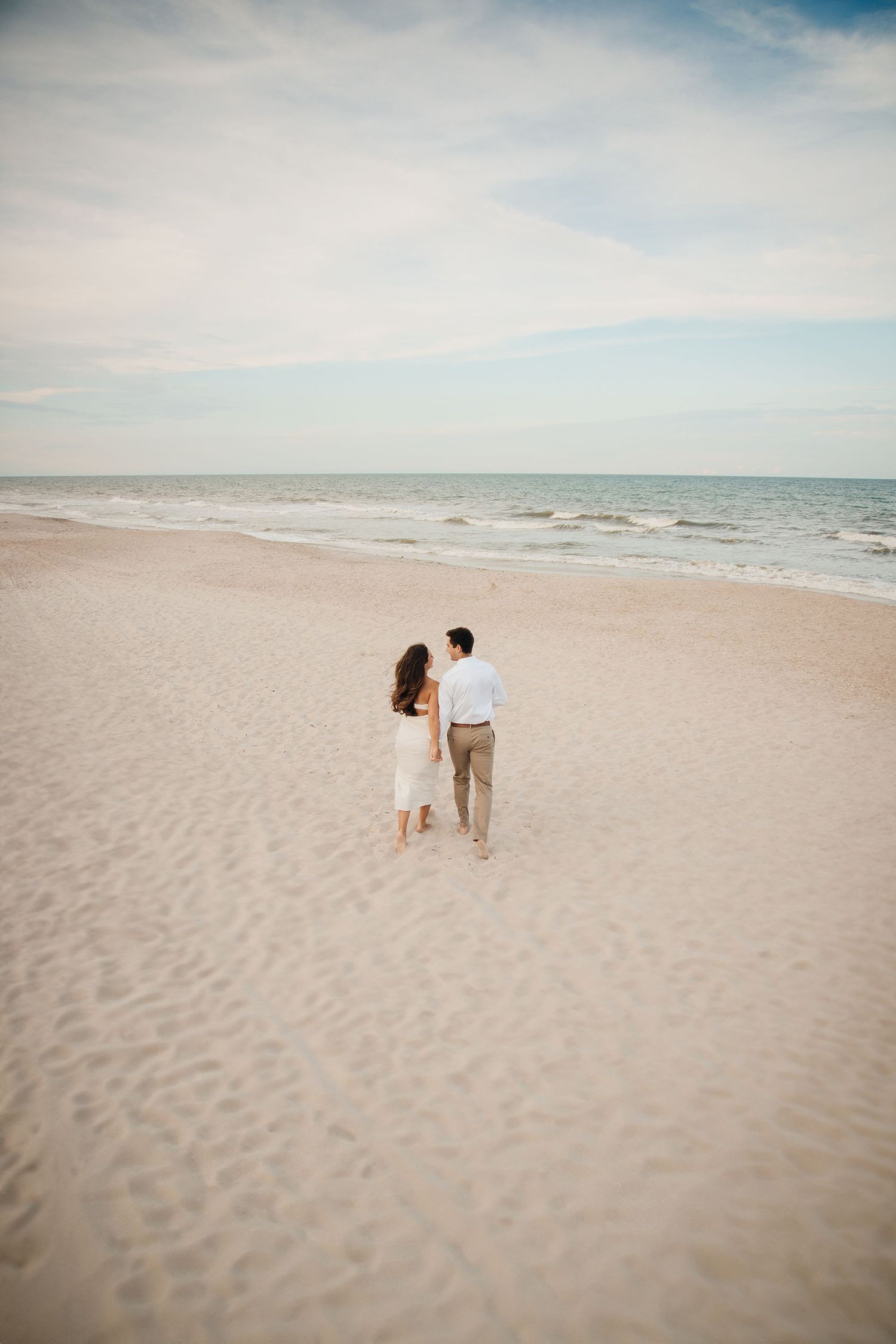 Distant view of a couple walking on an empty beach at sunset.