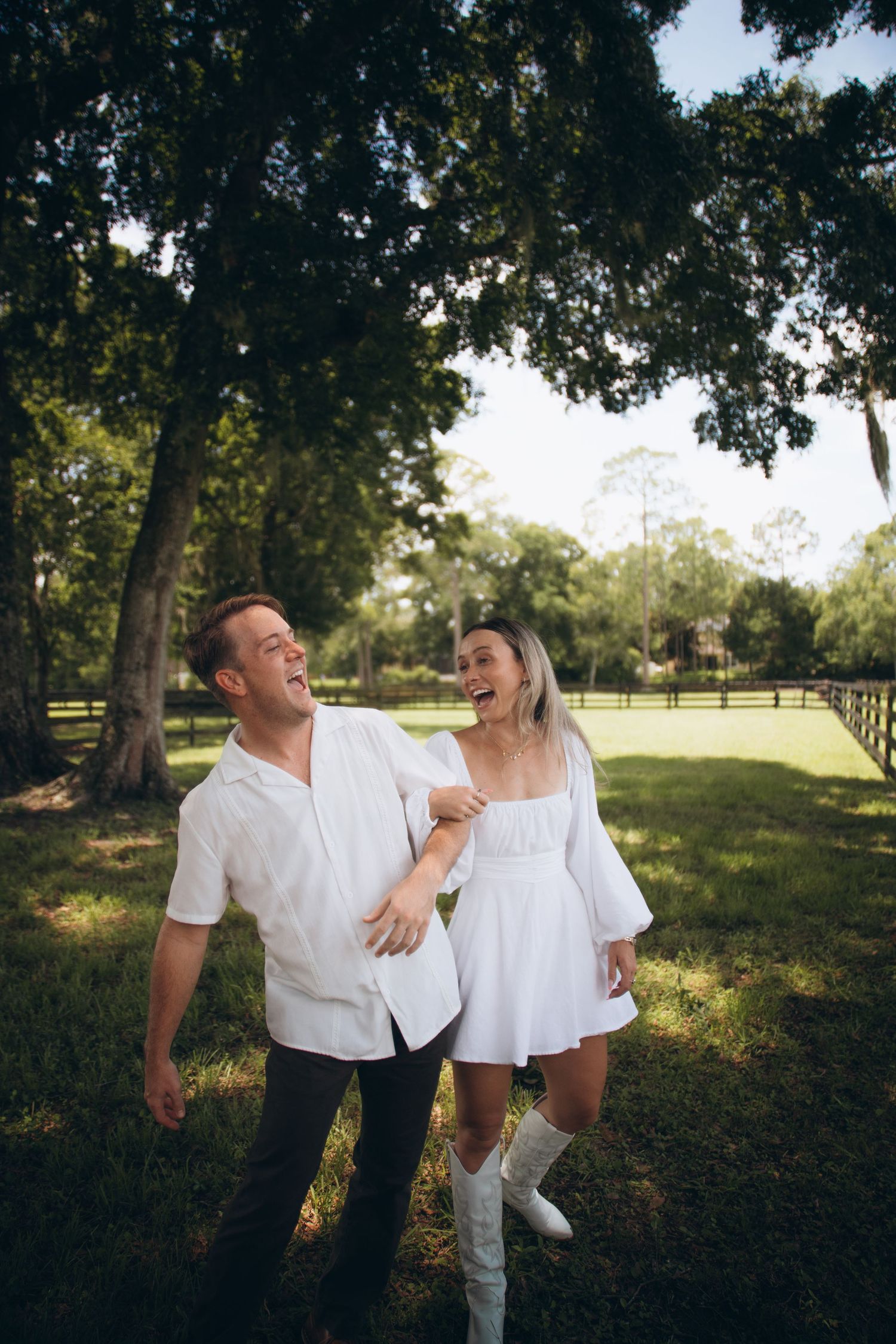 A joyful couple laughs together while walking through a scenic tree-lined field.