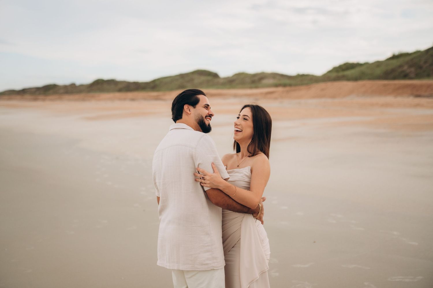 Couple sharing intimate moment on beach with coastal landscape in background.