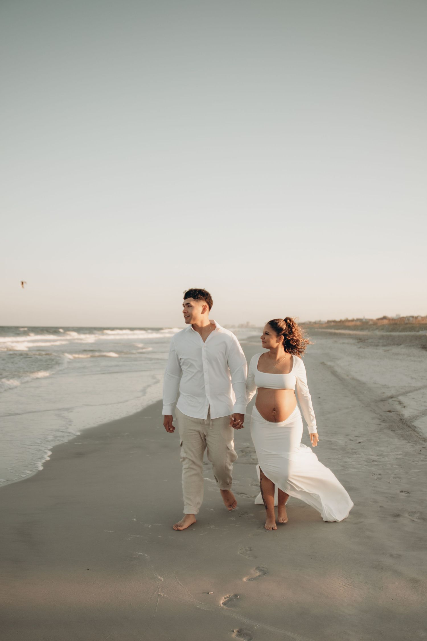 Couple walking hand in hand along the beach during their maternity photoshoot.