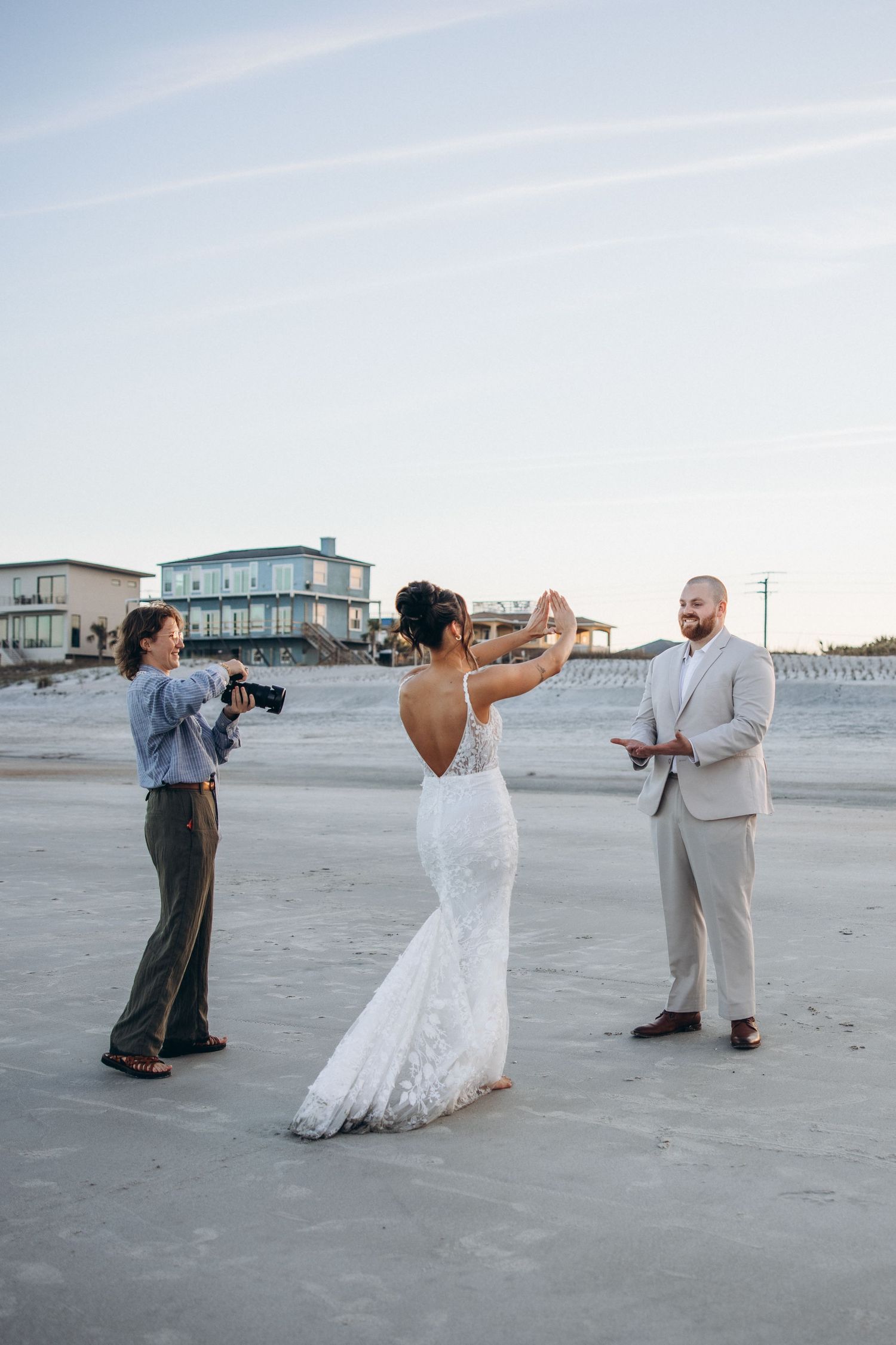 Bride and groom exchange vows on a sandy beach while a photographer captures the intimate outdoor wedding ceremony.