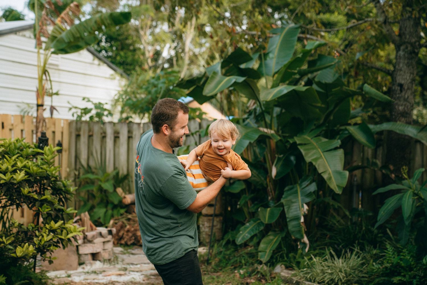 Family enjoying outdoor activities among tropical plants in fenced backyard.