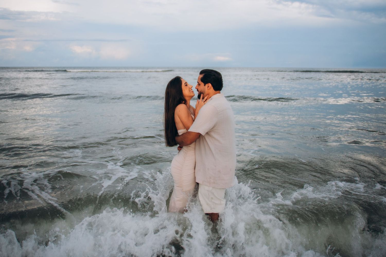 Romantic couple getting splashed by ocean waves while embracing on the beach.