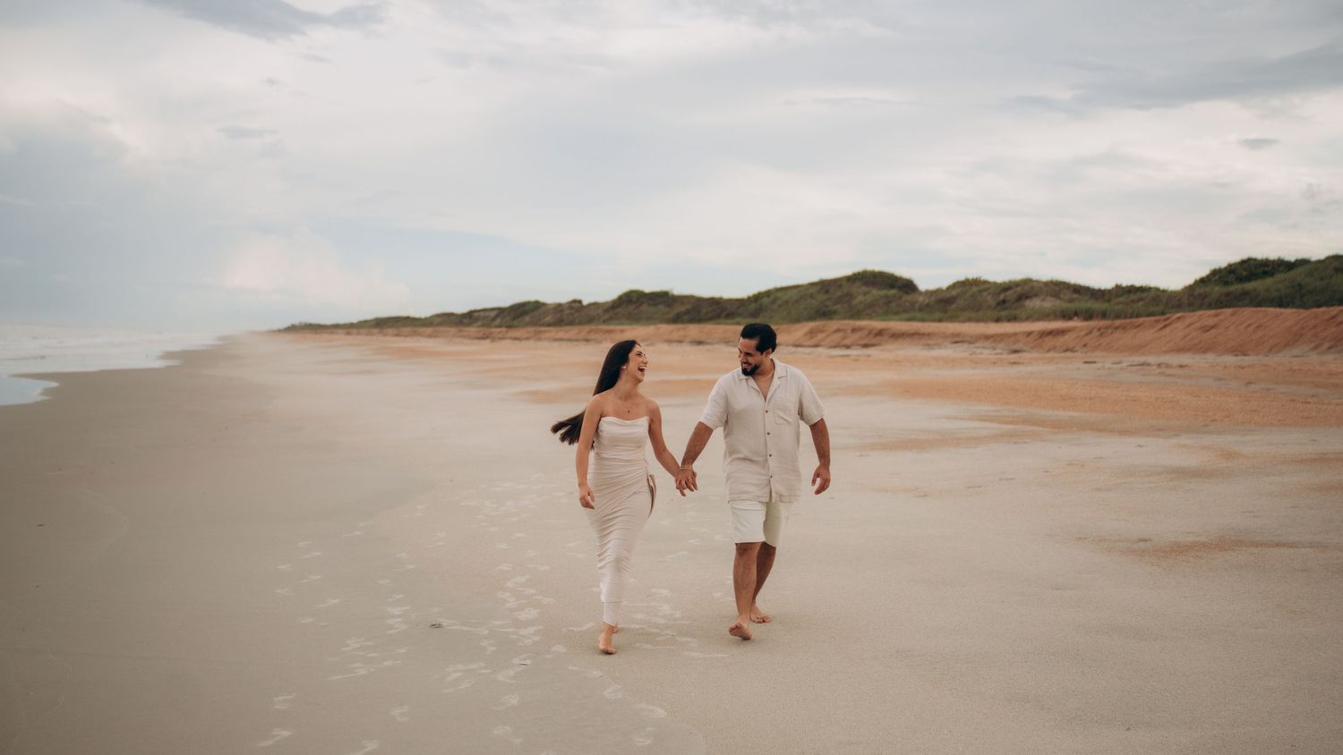 Romantic couple walking hand in hand along a serene beach during sunset.