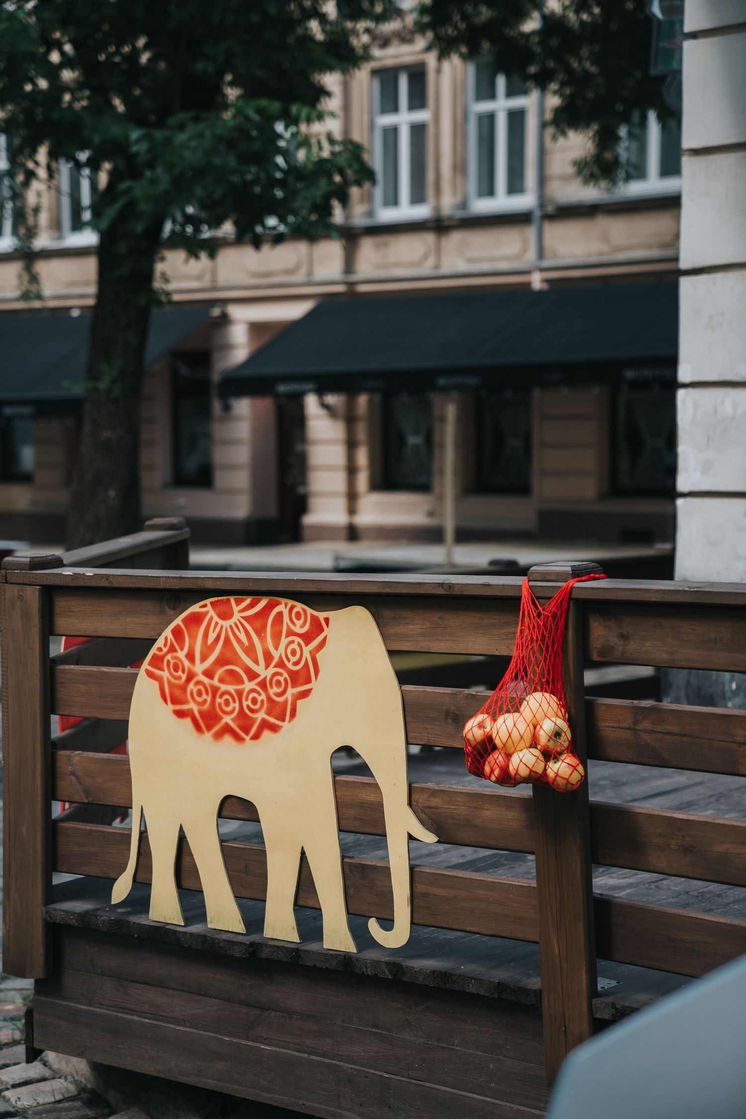 Decorative wooden elephant cutout with red mandala design displayed on a fence at an outdoor cafe.