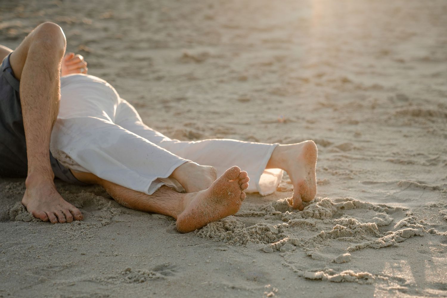 Two people lying close together on sandy beach during sunset.