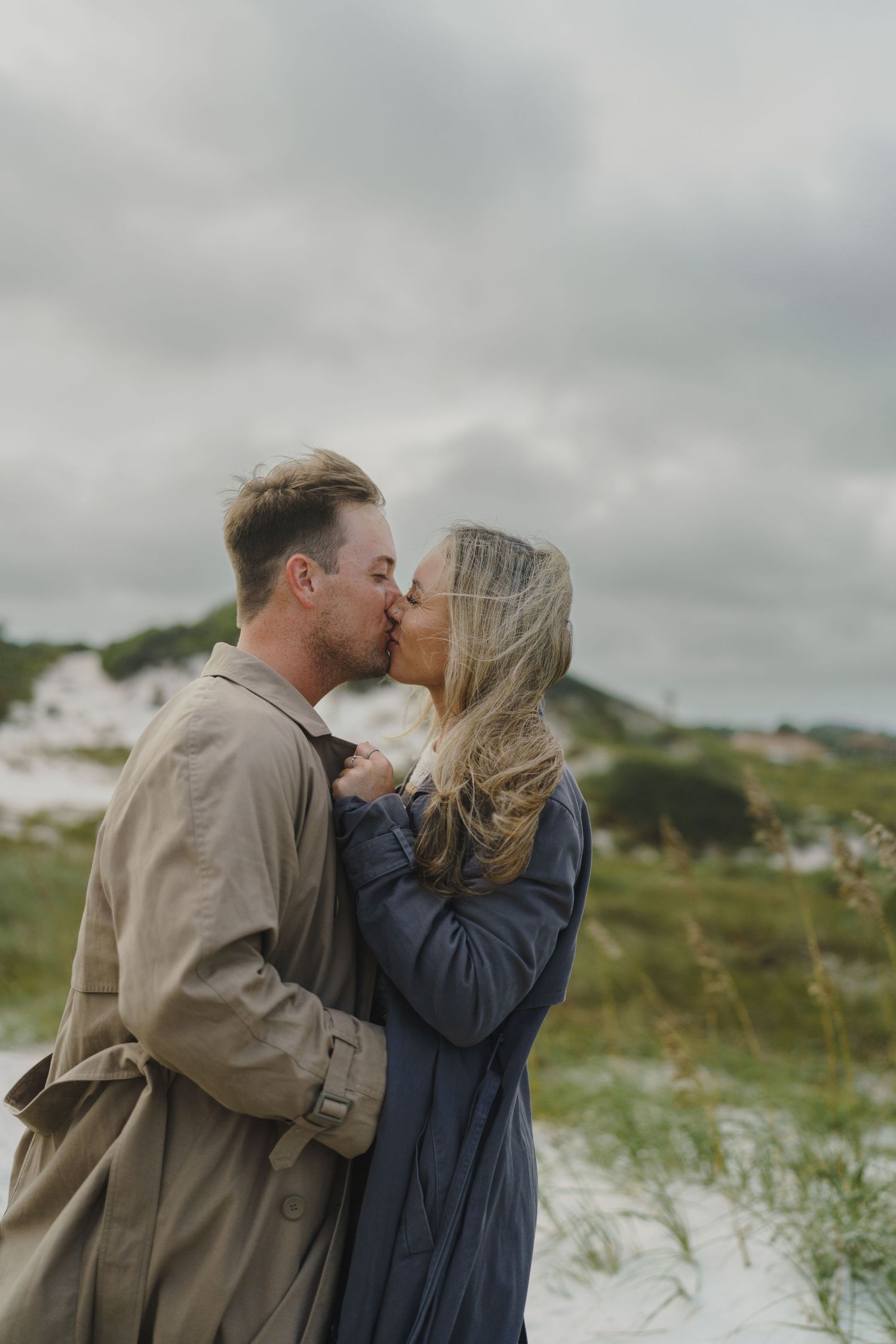 A couple shares a romantic moment among the beach dunes with sea grass swaying in the wind.