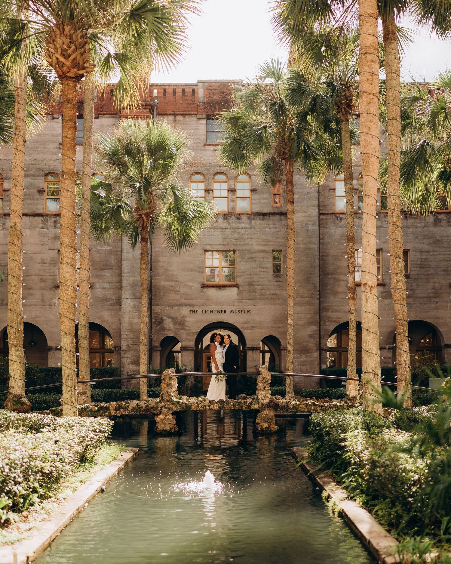 A scenic courtyard with palm trees and a reflecting pool surrounded by Spanish colonial architecture.