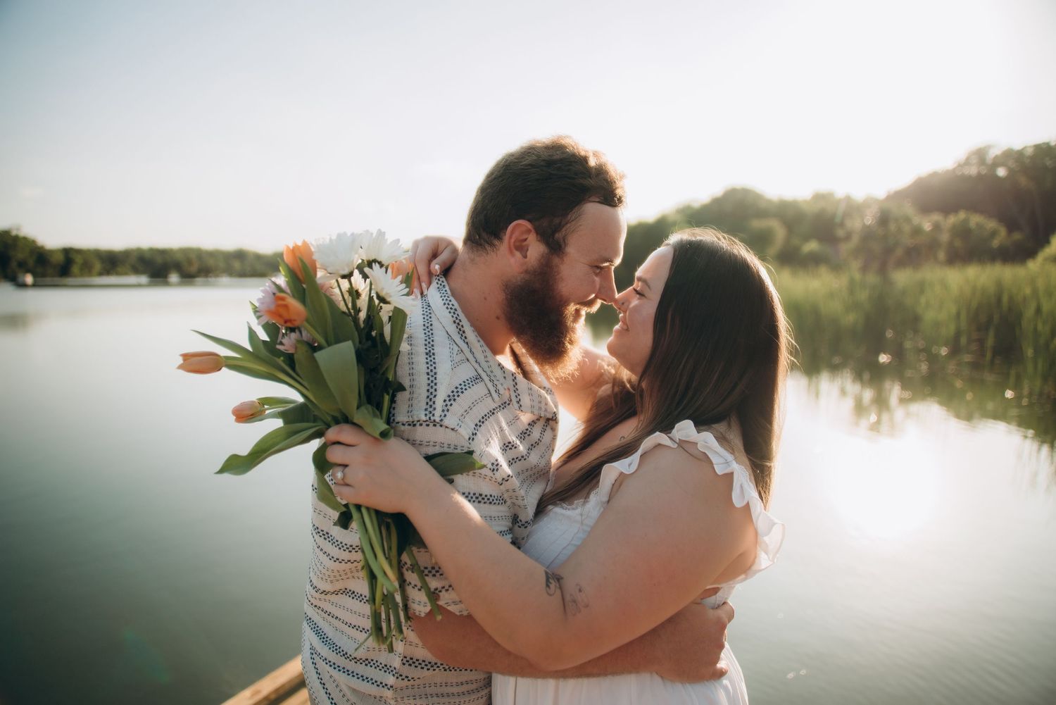 A romantic lakeside photoshoot with a couple embracing near the water at sunset.