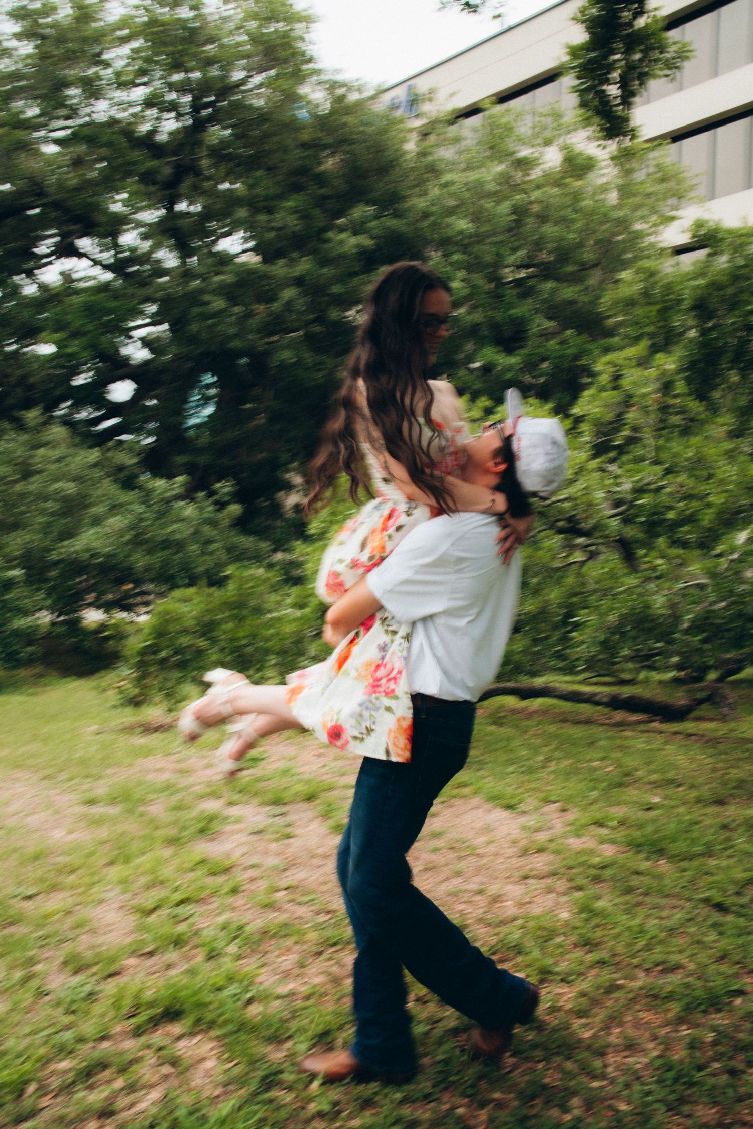 Couple sharing joyful moment as man lifts woman in floral dress spinning in lush green park.