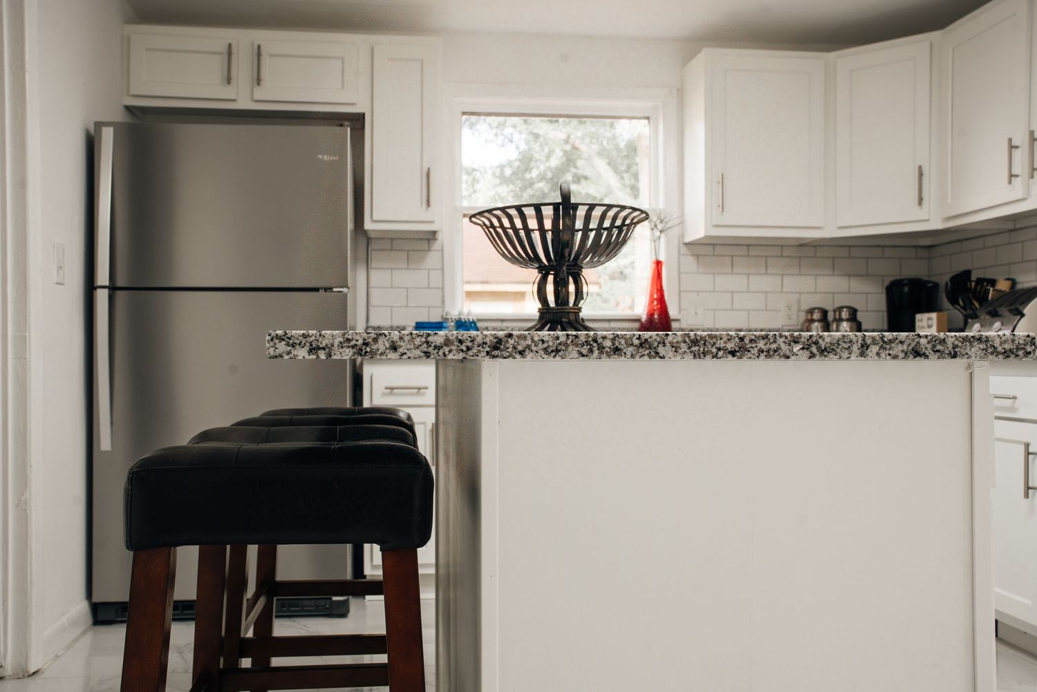 Modern white kitchen with granite island, stainless steel fridge, subway tile backsplash, and bar stool.