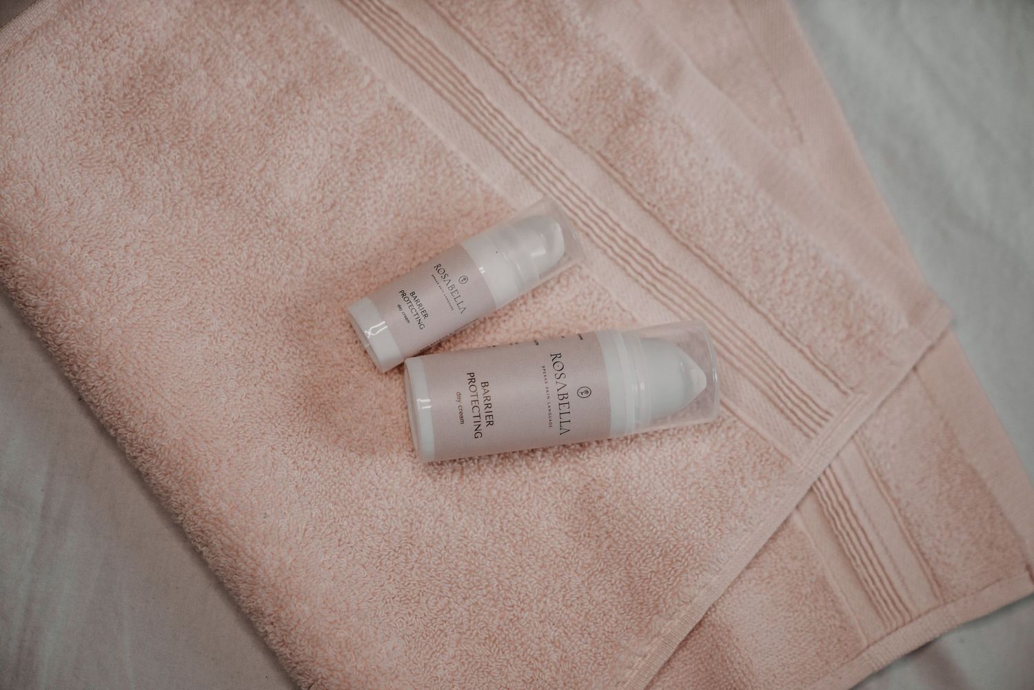 Two small white lotion bottles resting on a soft pink terry cloth towel.