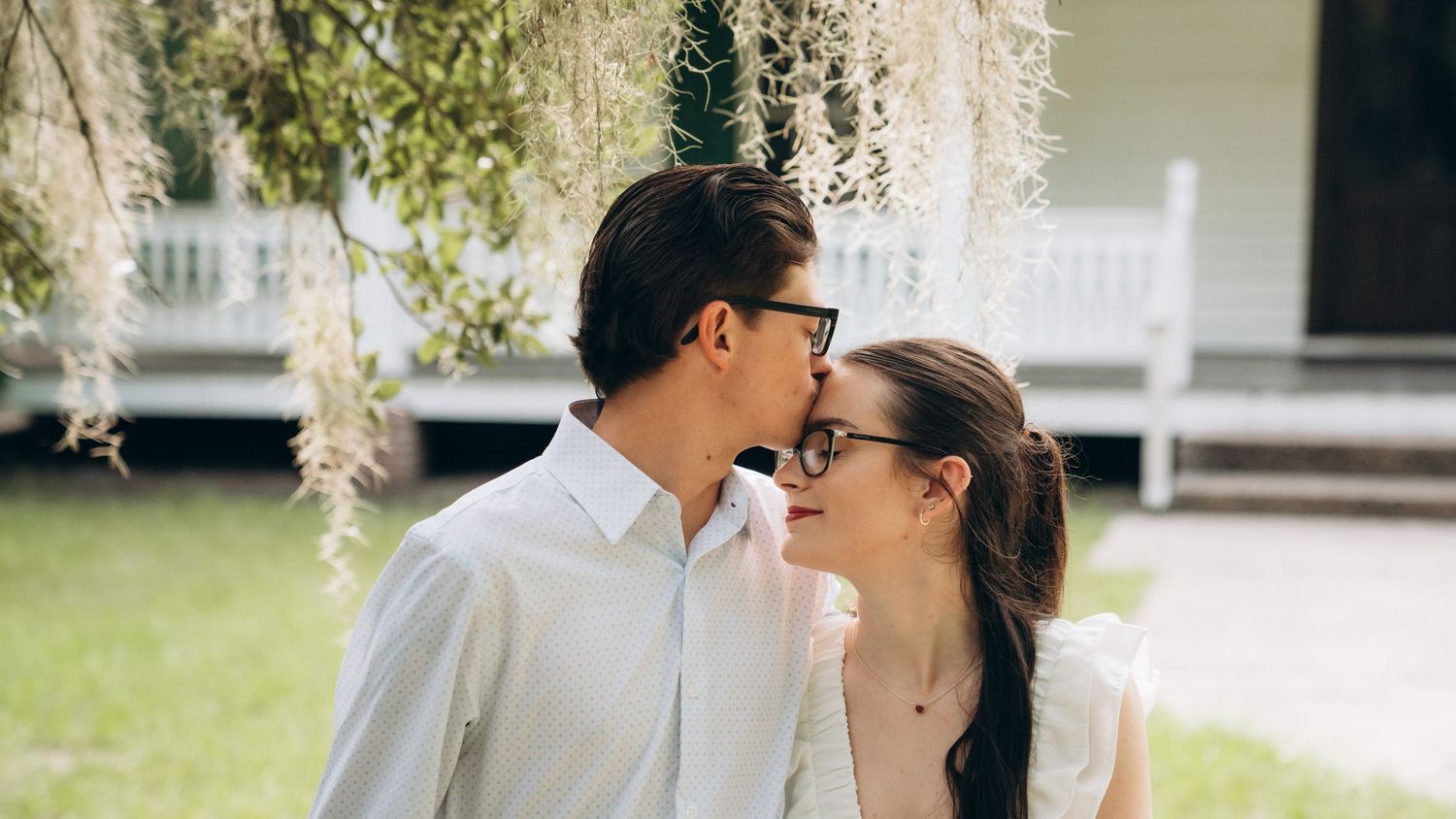 A tender moment shared between a couple in white clothing against a rustic backdrop.