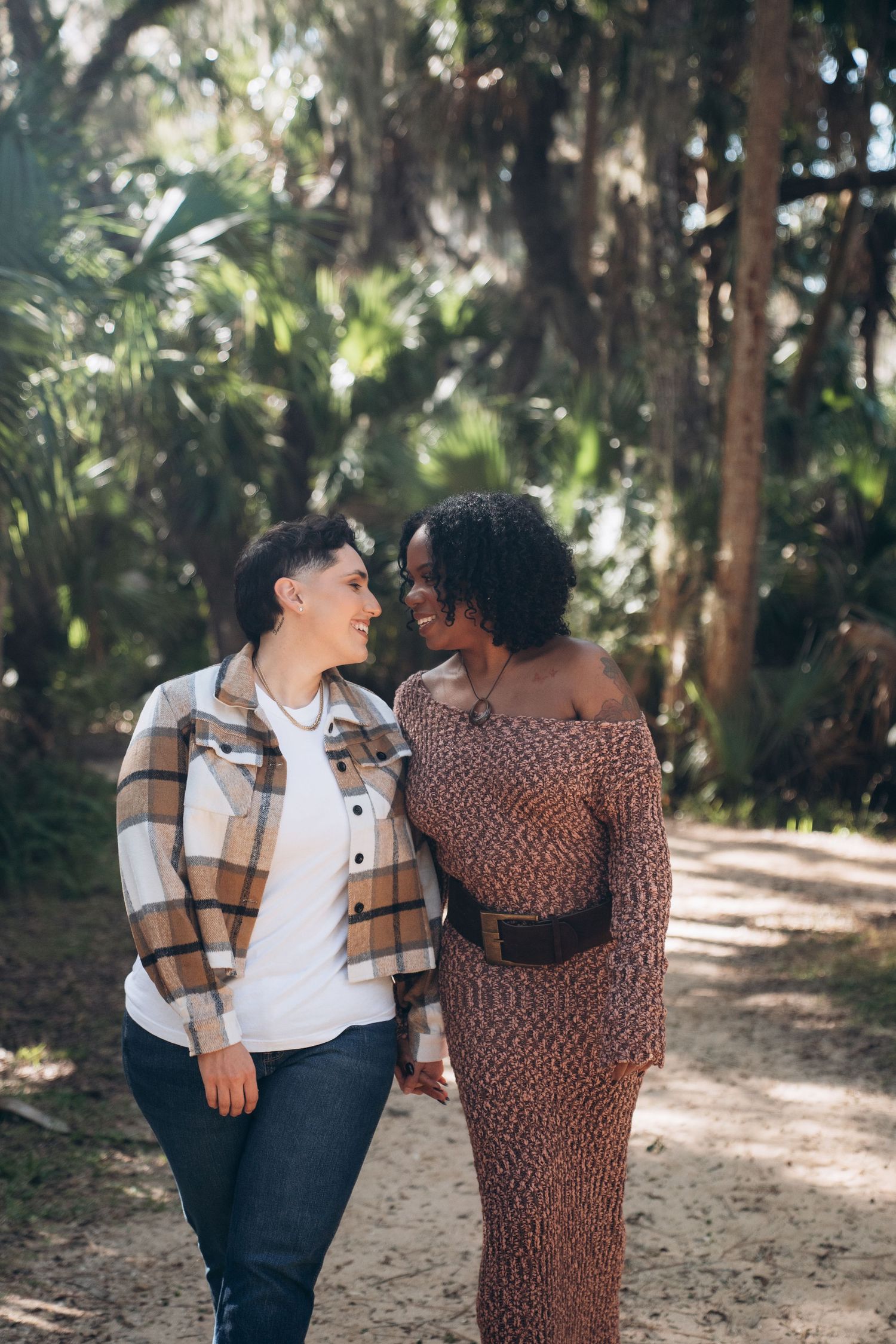 A couple shares tender moments together while walking along a tree-lined path on a sunny afternoon.