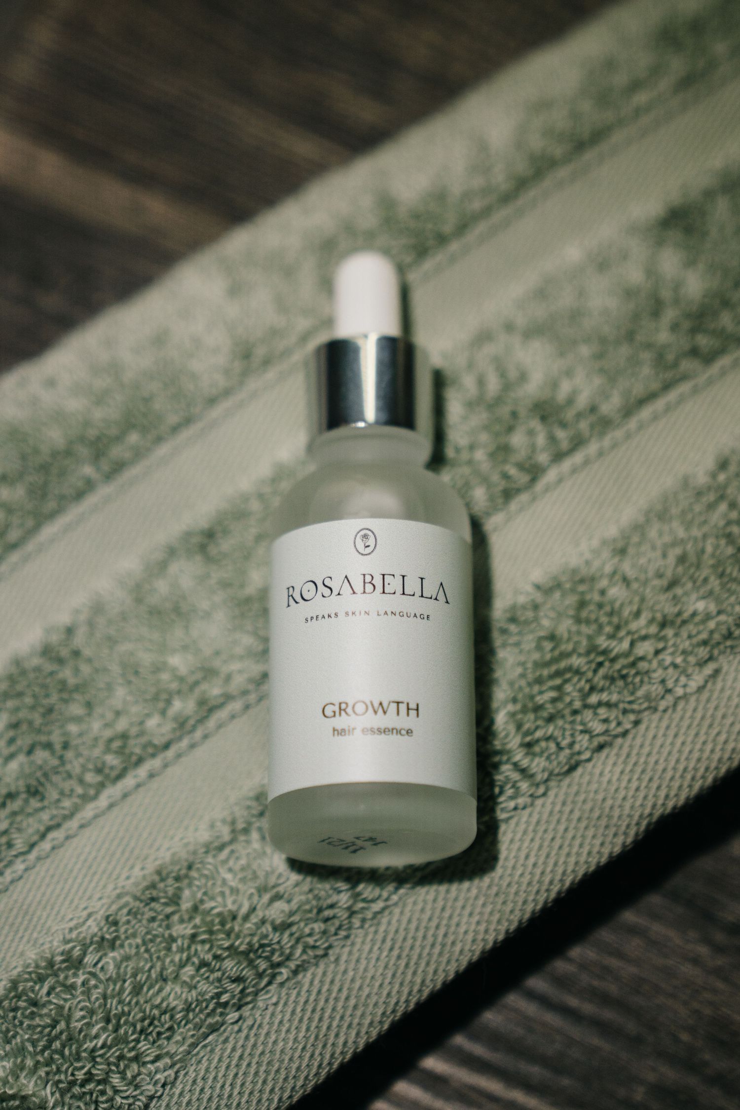 Rosabella Growth face serum dropper bottle resting on a green towel in natural sunlight.