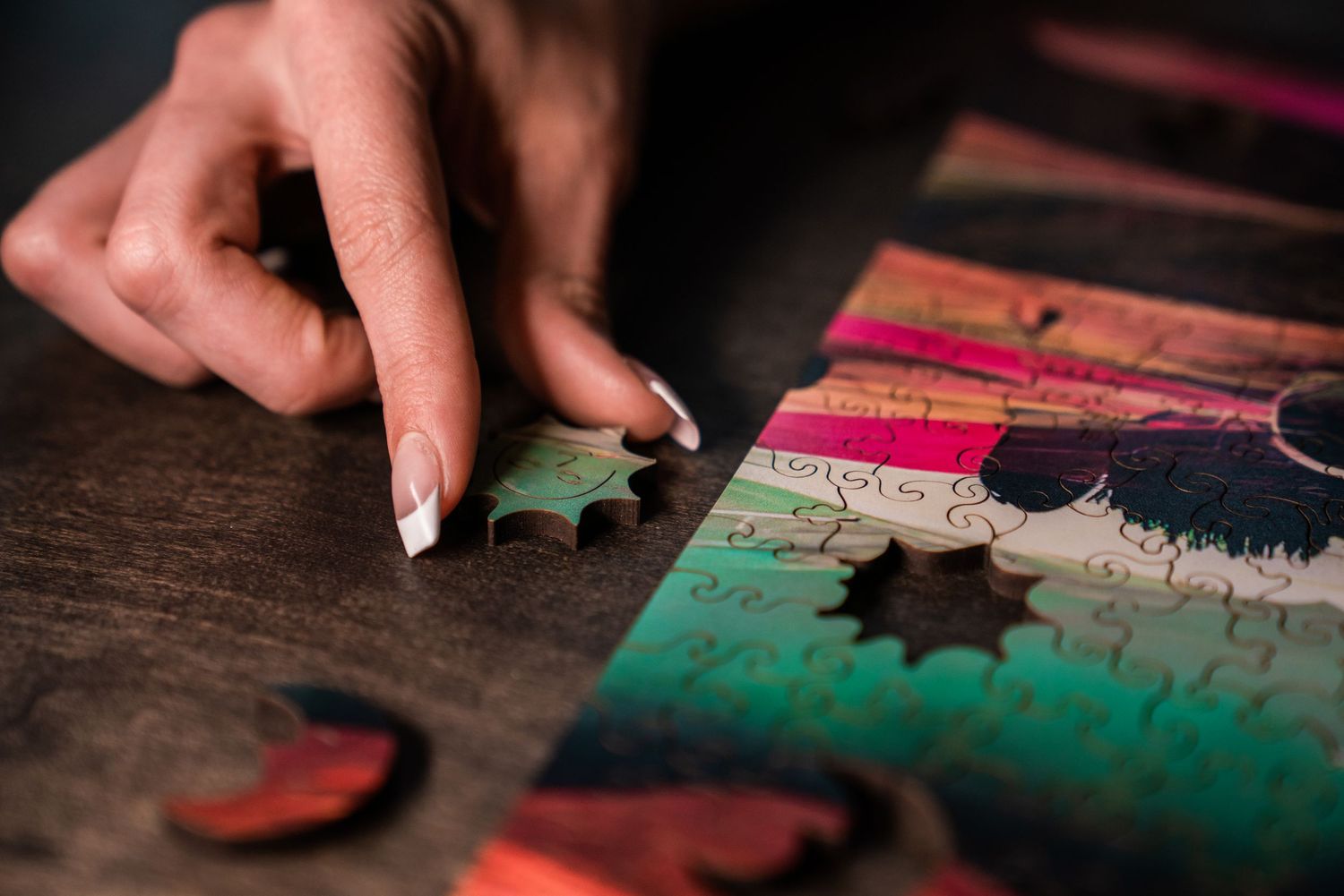 Close-up of a hand placing a wooden puzzle piece onto a colorful assembled jigsaw puzzle.