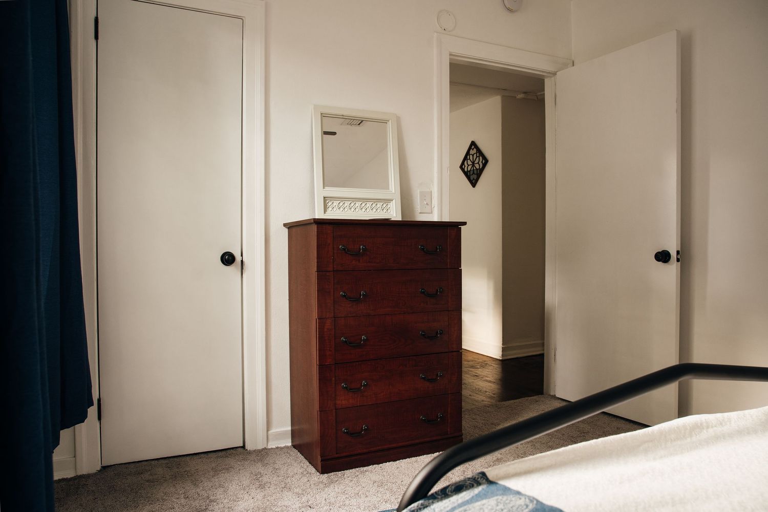 Bedroom corner with wooden dresser, mirror, and two white doors in a cozy carpeted room.
