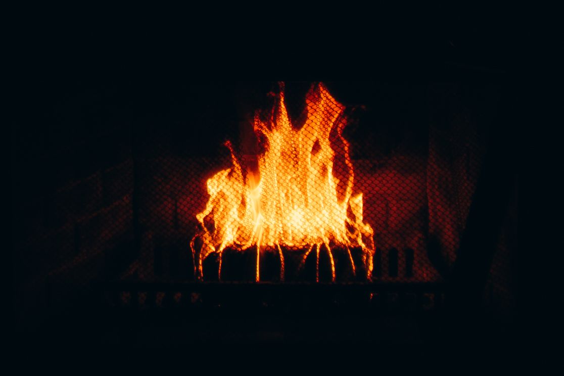 Bright orange and yellow flames burning intensely in a dark fireplace with glowing embers on logs.