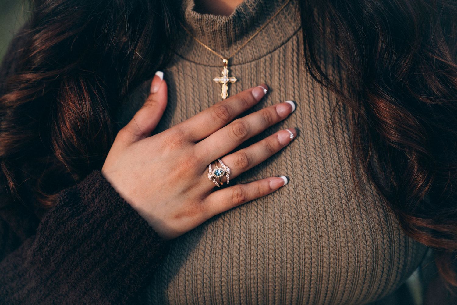 A couple holds hands and shows off an engagement ring in a warm, intimate indoor setting.
