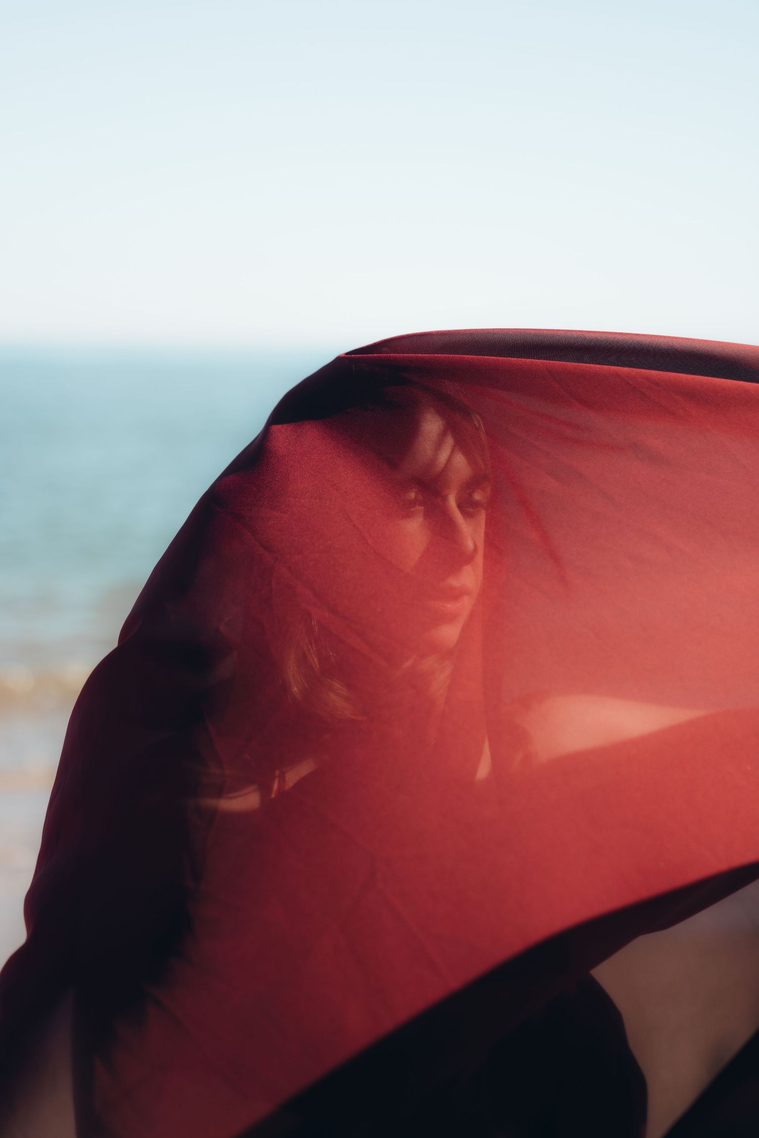 Red fabric billowing in the wind against a bright coastal backdrop.