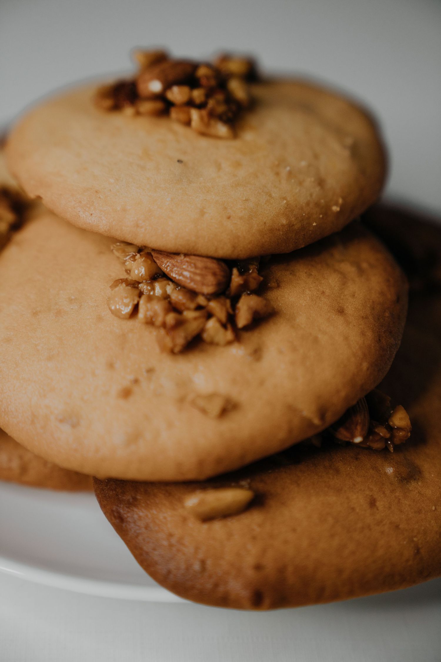 Stack of three round almond cookies topped with chopped nuts on a white plate.
