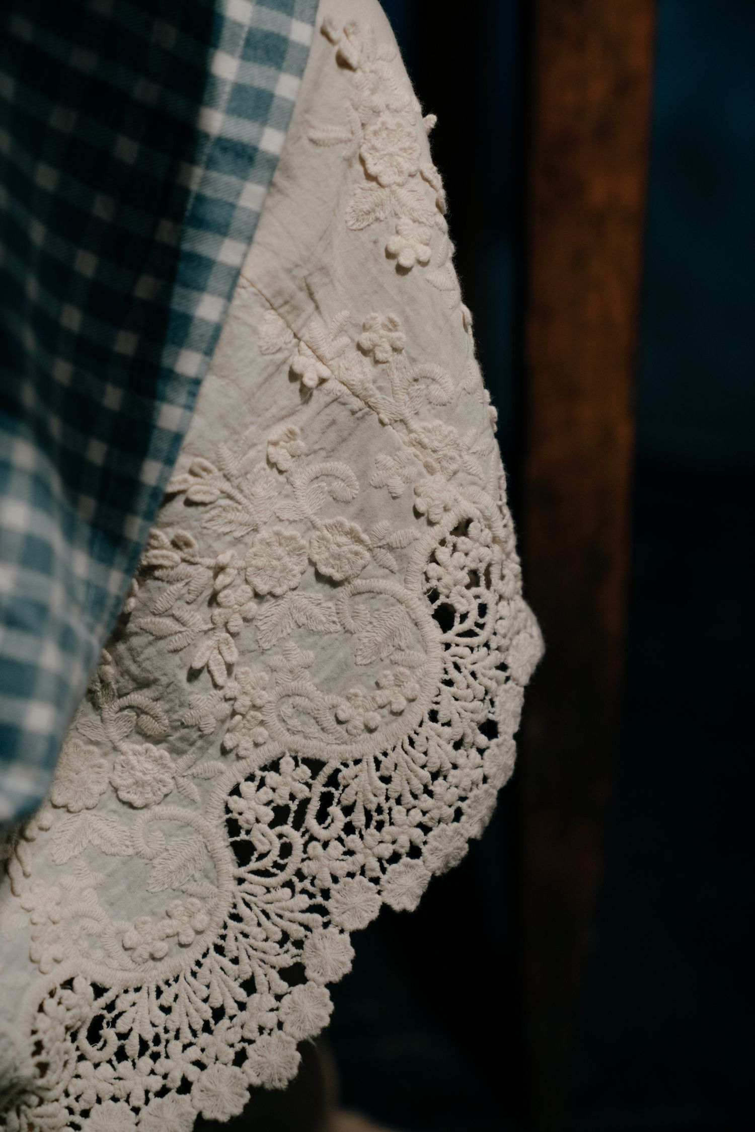 Delicate white lace doily with floral embroidery draped over a blue gingham cloth.