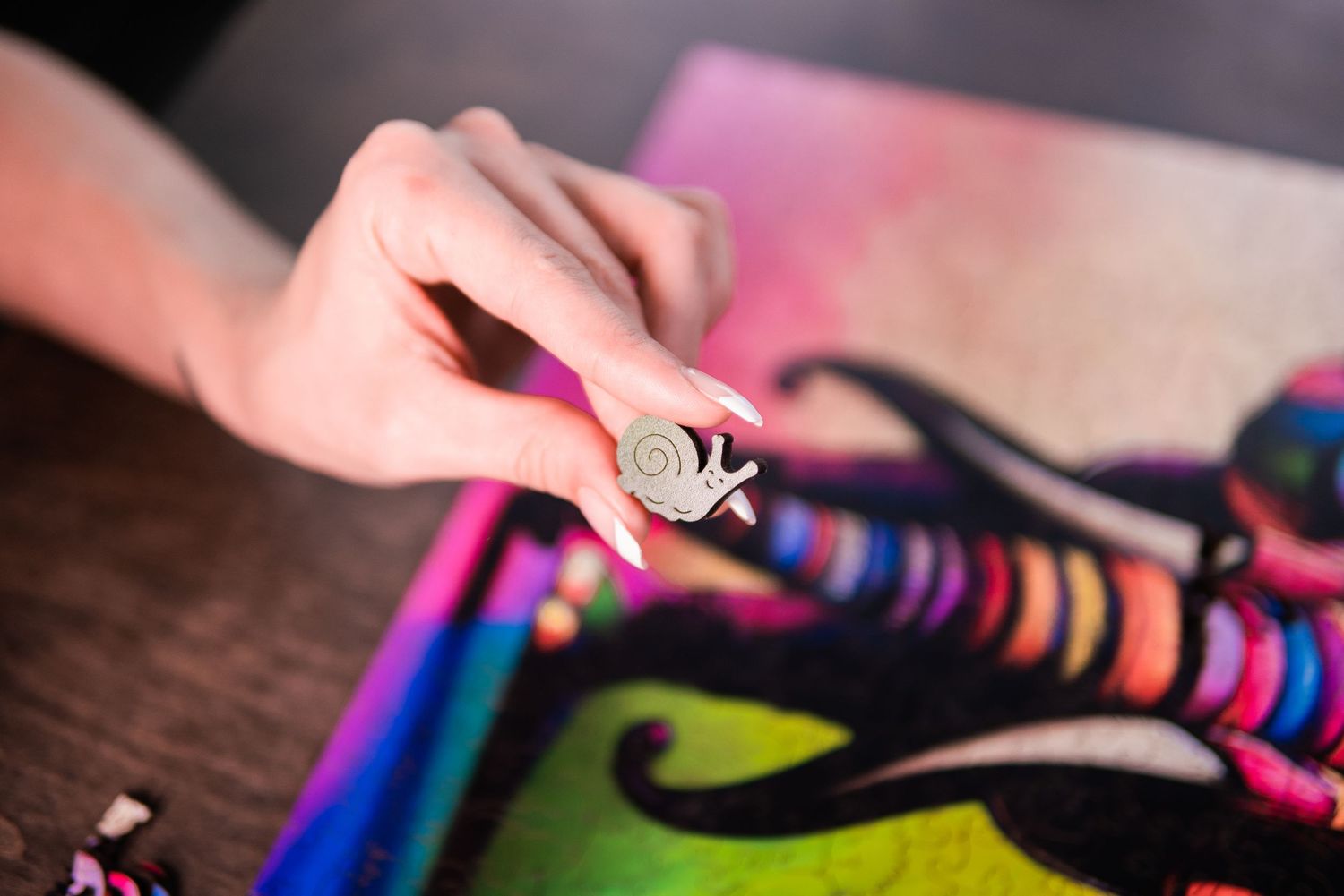 Hand holding a small snail figurine over colorful felt art on a wooden table.
