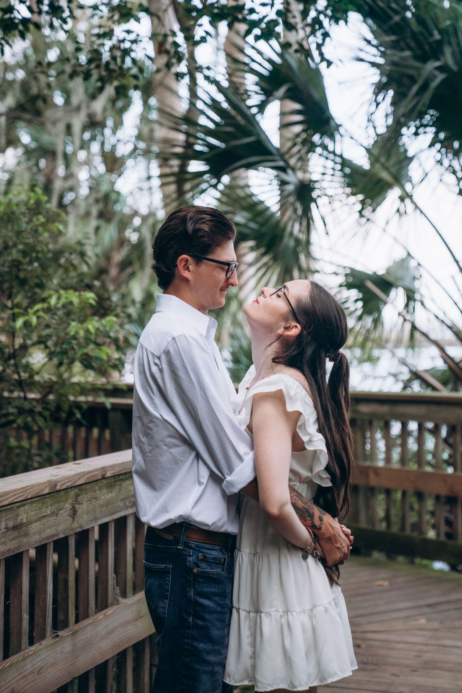 Couple sharing romantic moment on wooden deck surrounded by palm trees.