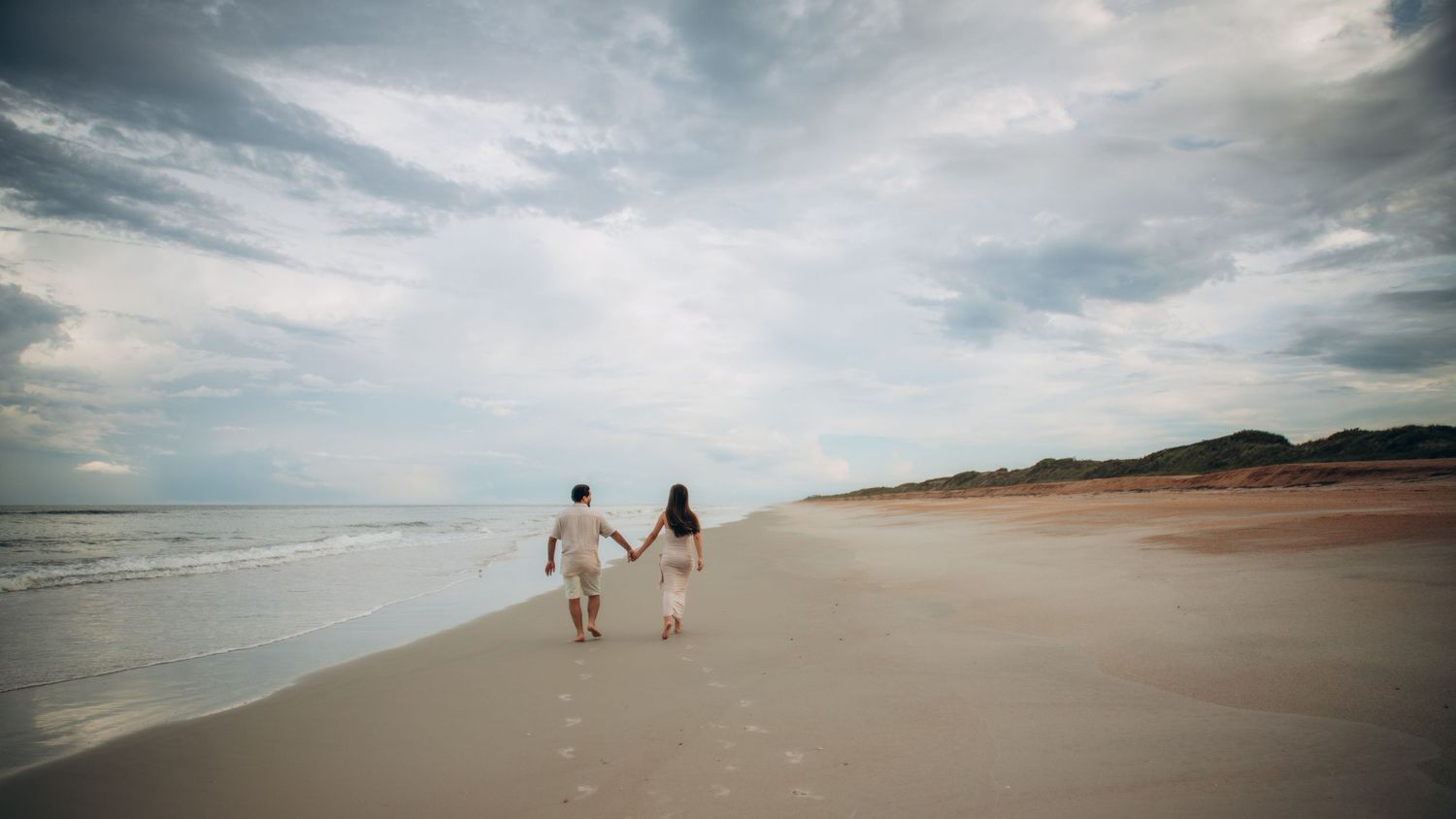 Panoramic view of a cloudy beach landscape with rolling waves and sandy shores stretching into the distance.