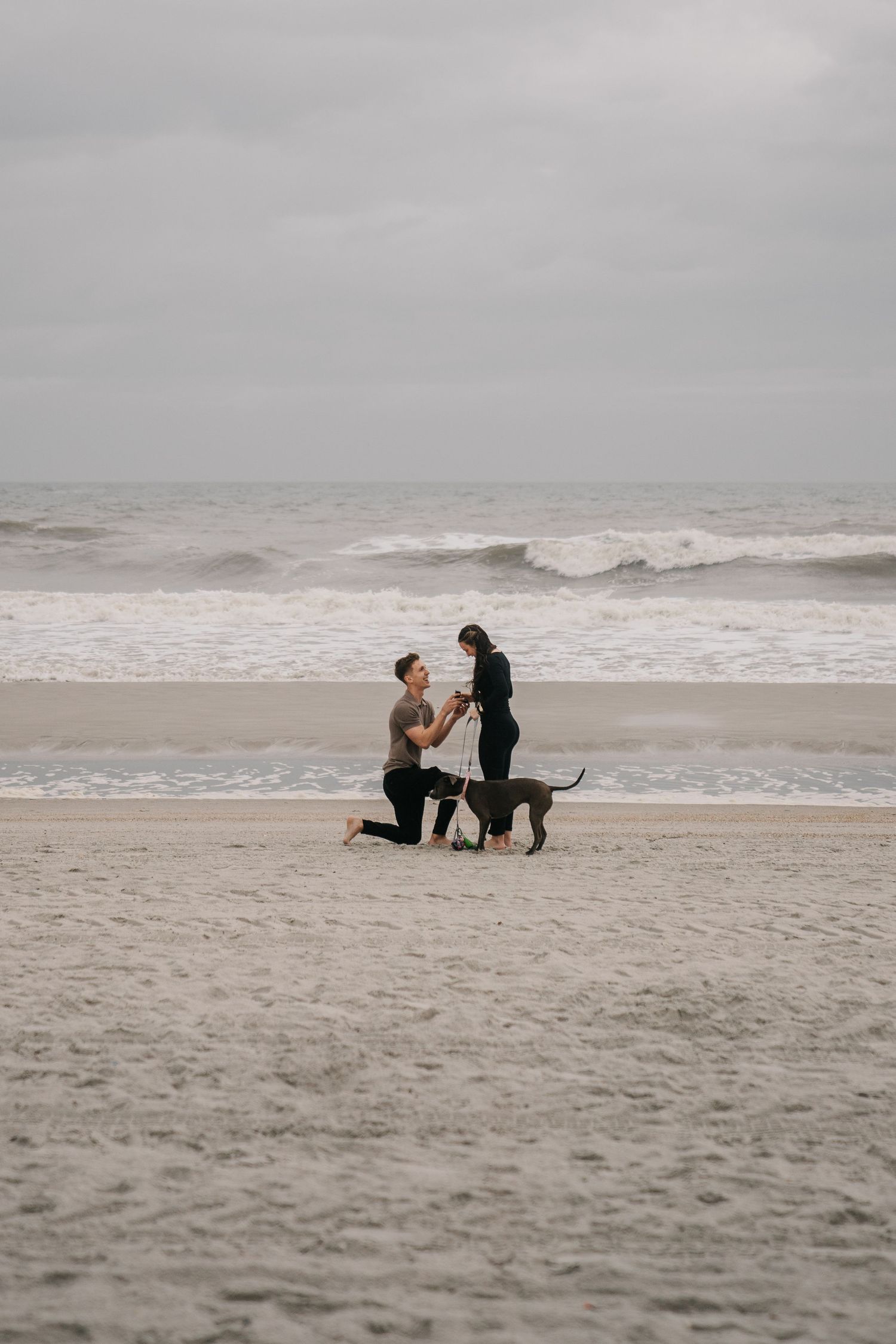A couple sits together on a misty beach with waves crashing in the background.