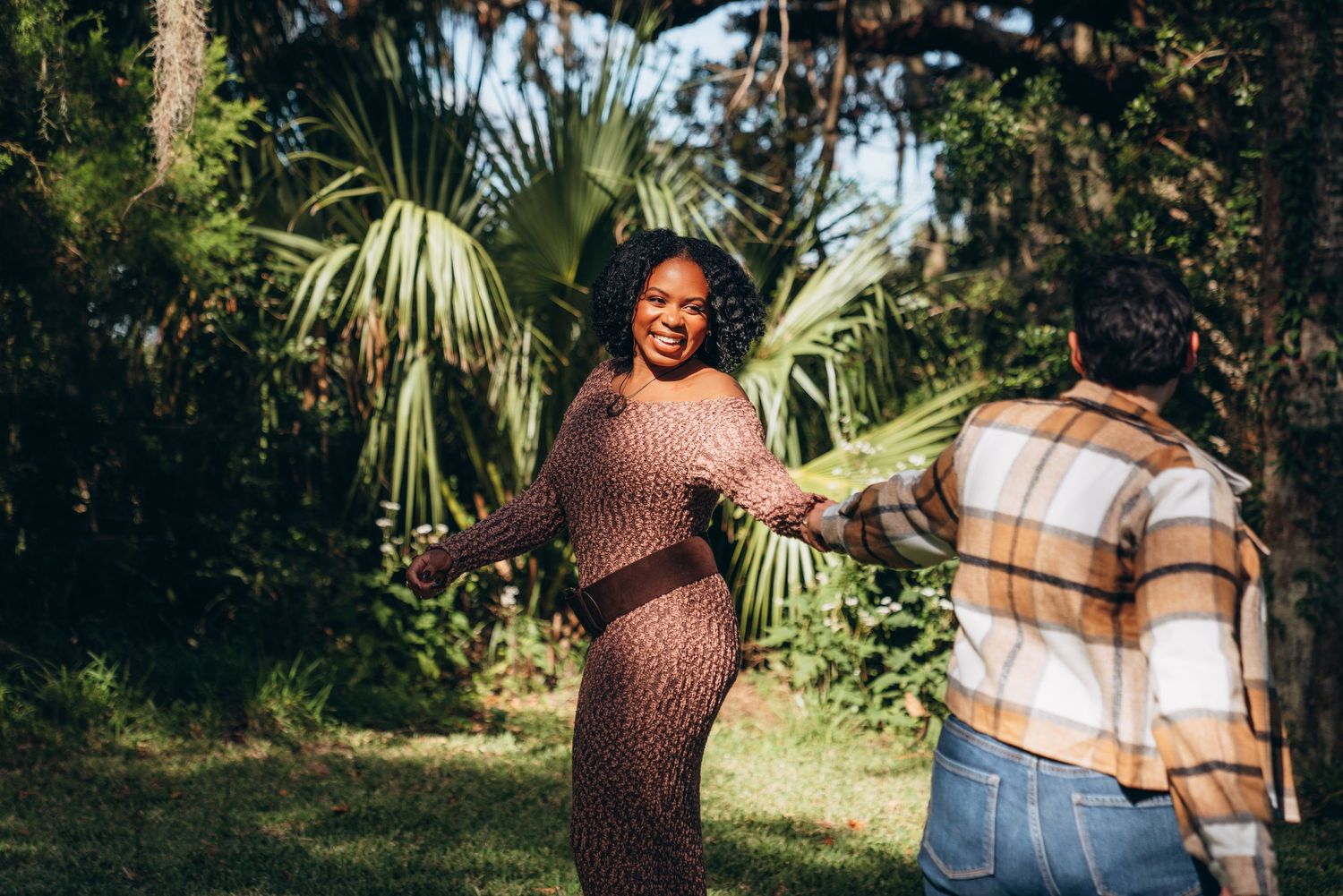 Affectionate couple embraces in a tropical garden setting surrounded by palm fronds.