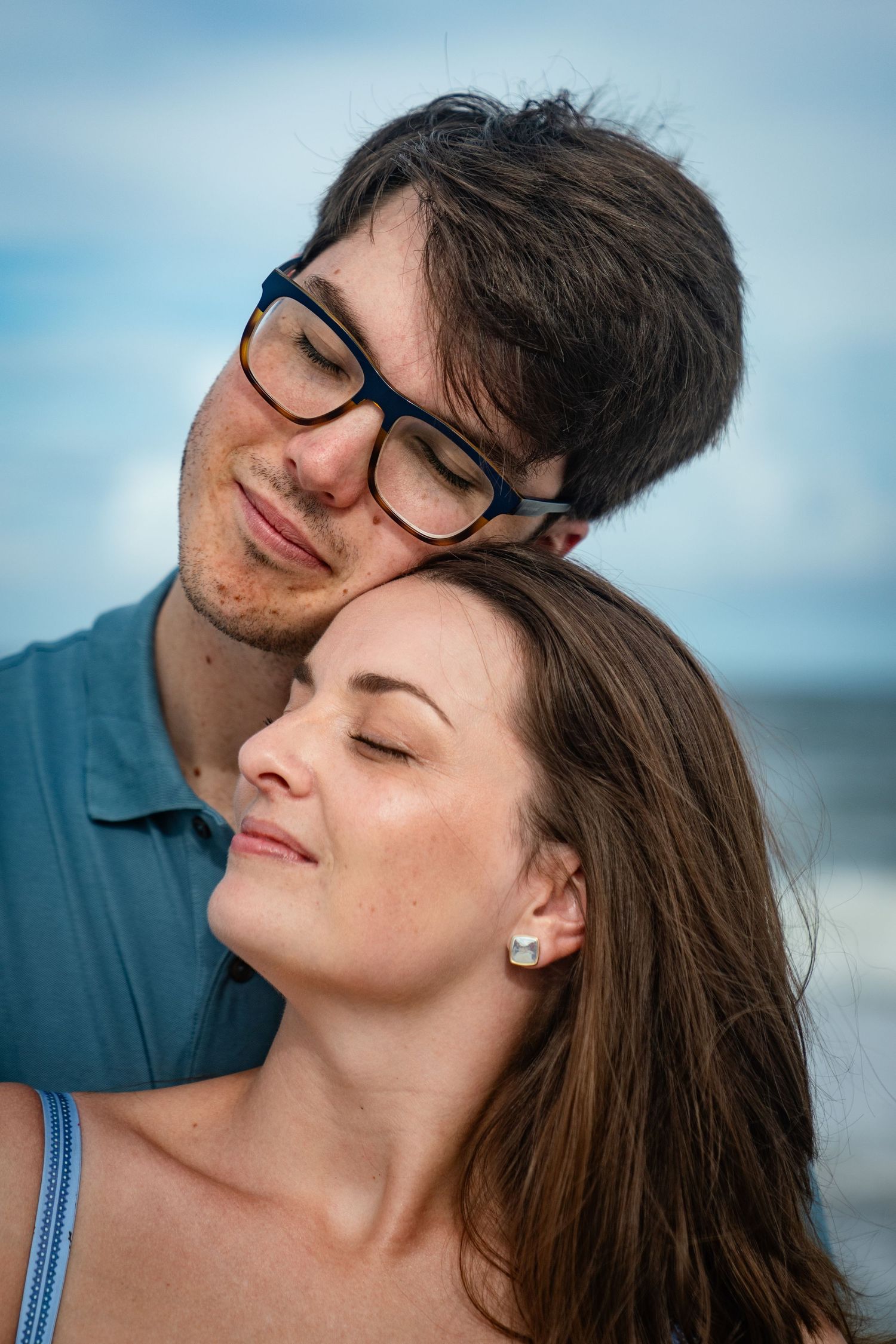 Close-up view of a romantic couple sharing an intimate moment with their eyes closed against a blue sky backdrop.