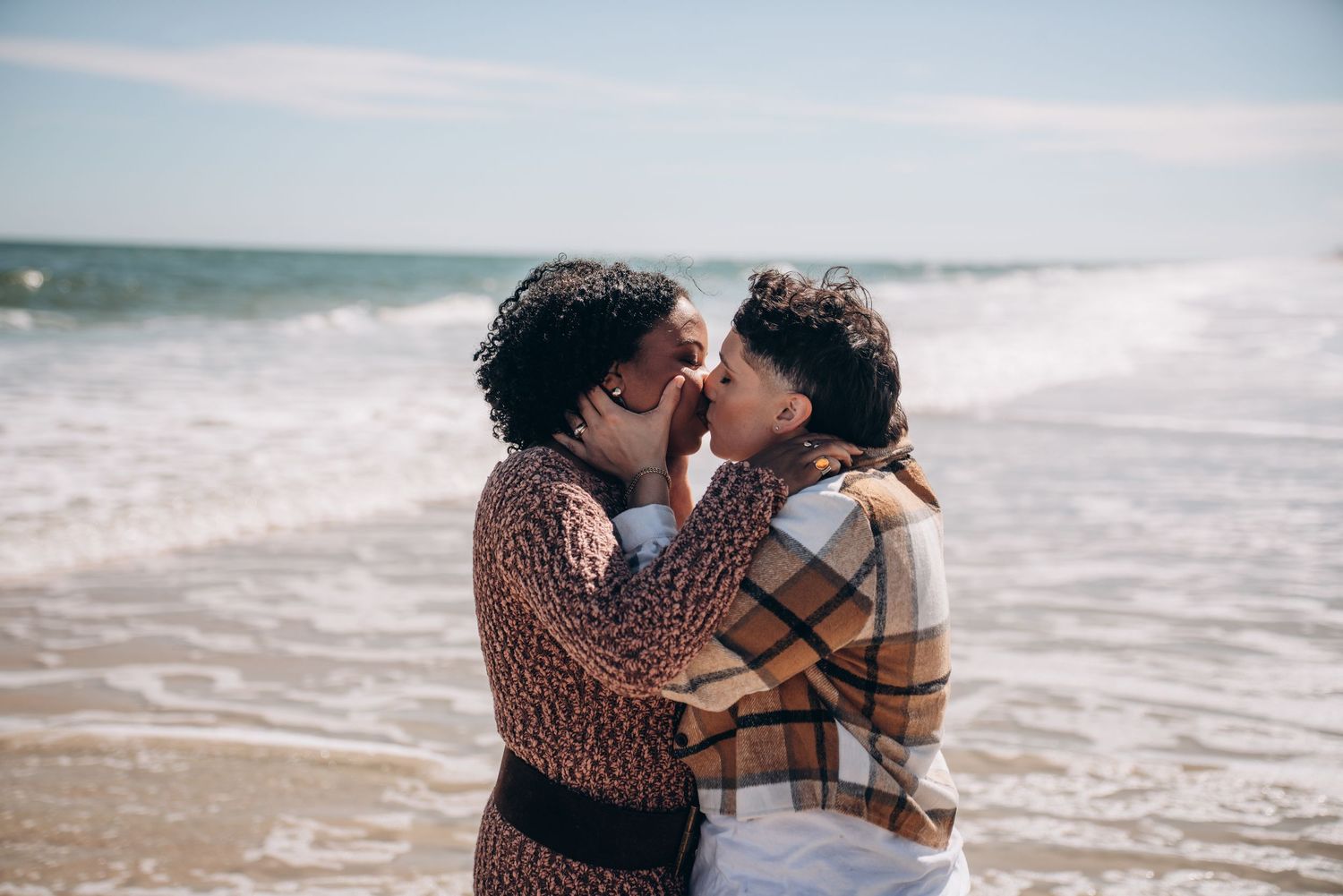 Couple embracing on a beach with ocean waves and blue sky in the background.