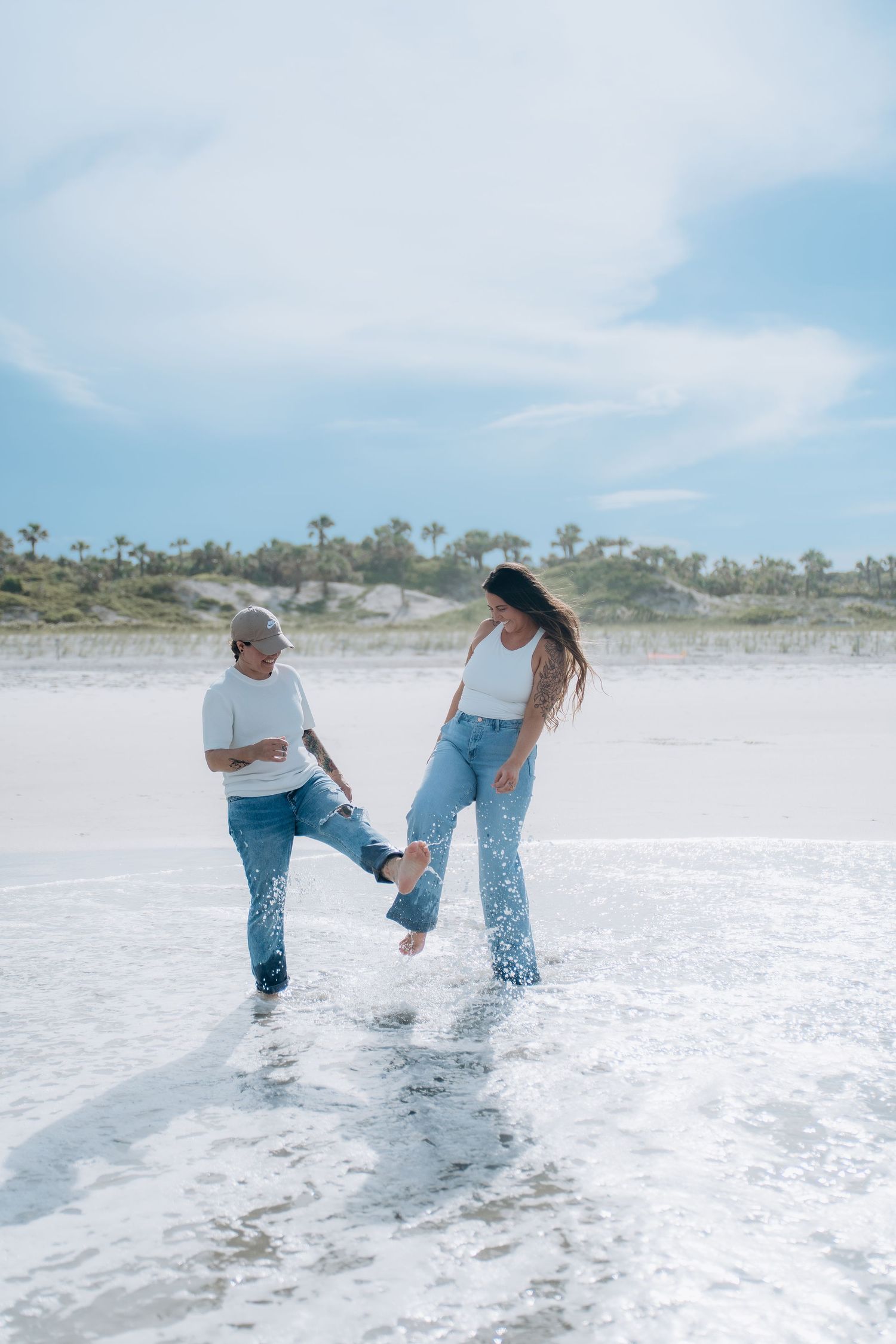 Two people splashing and playing in the ocean waves wearing matching outfits.