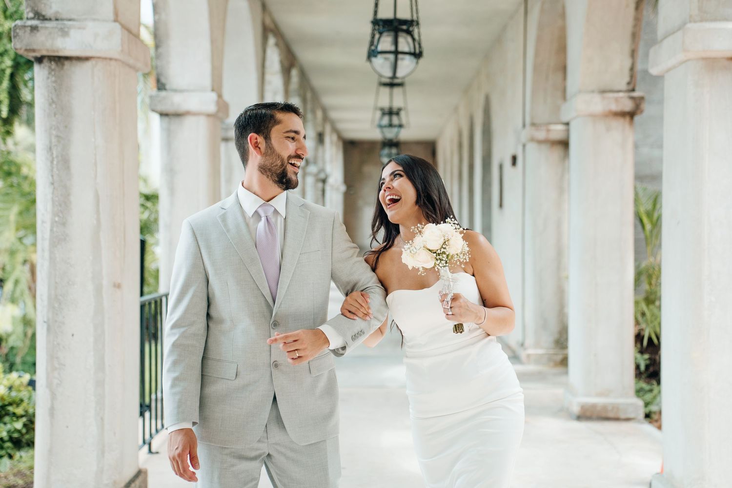 An elegant wedding photoshoot under a white columned archway with hanging lanterns.